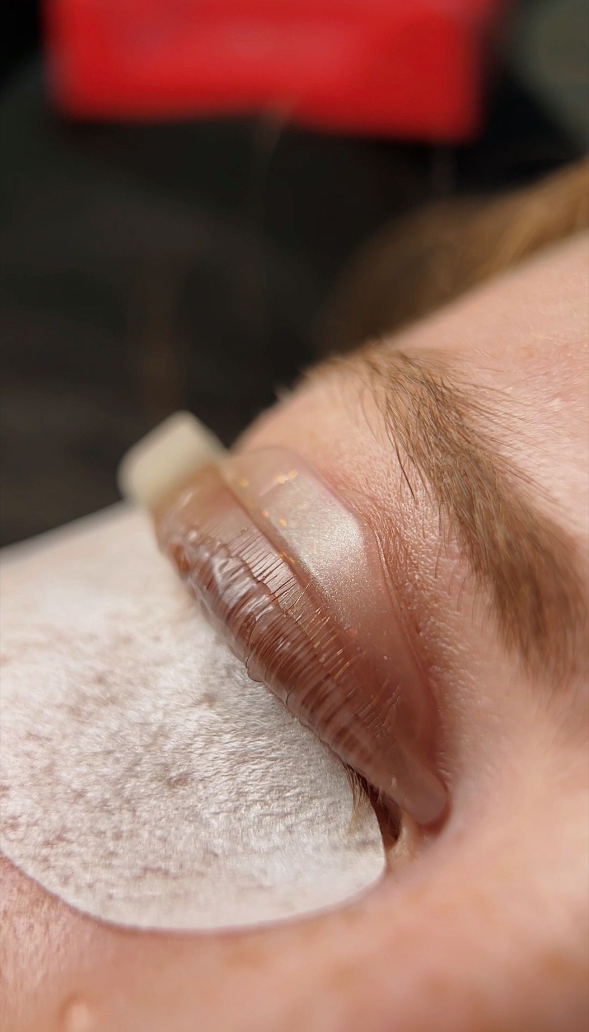 Woman receiving a lash lift with light pink pads on her eyelids and white under-eye patches.