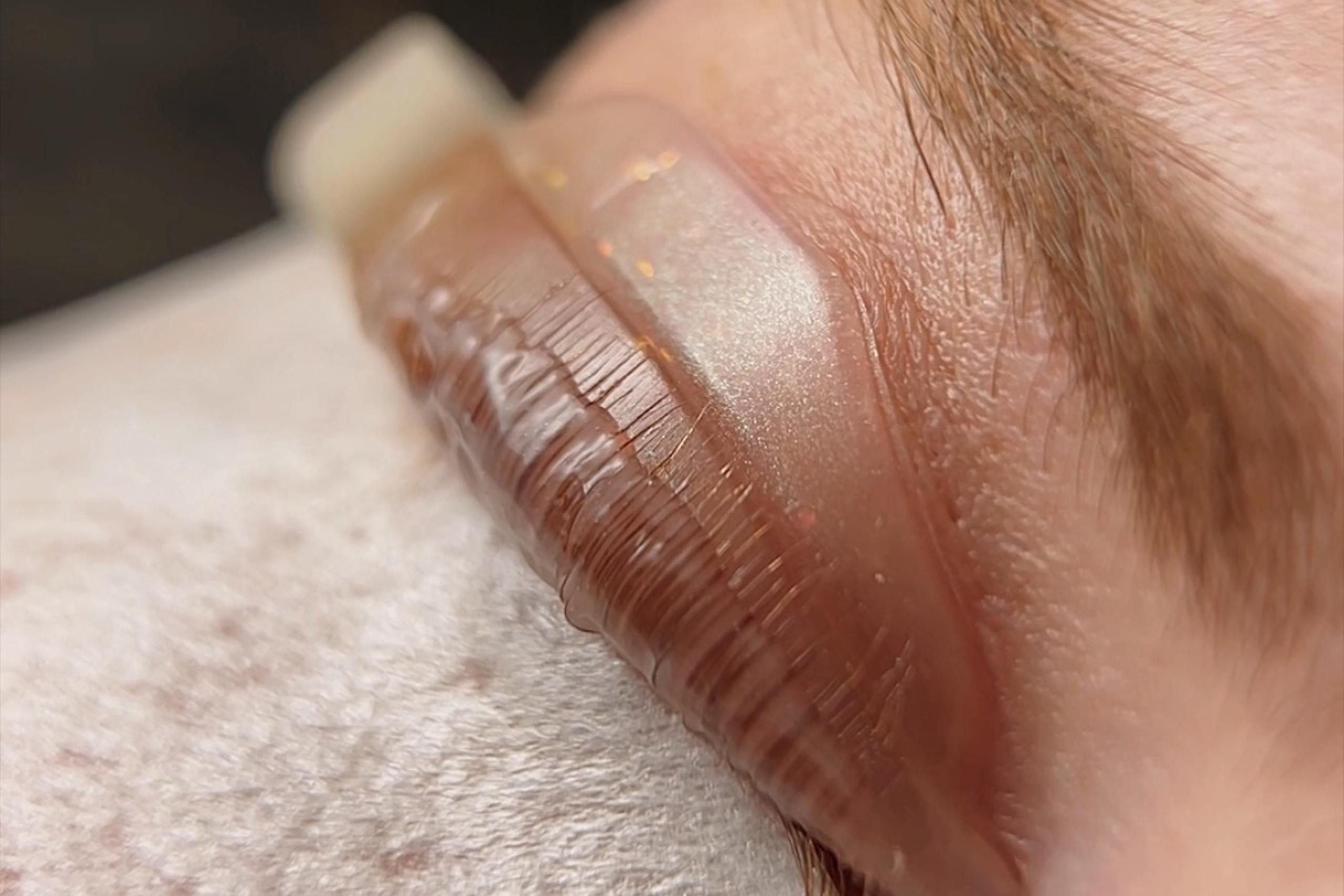 Woman receiving a lash lift with light pink pads on her eyelids and white under-eye patches.