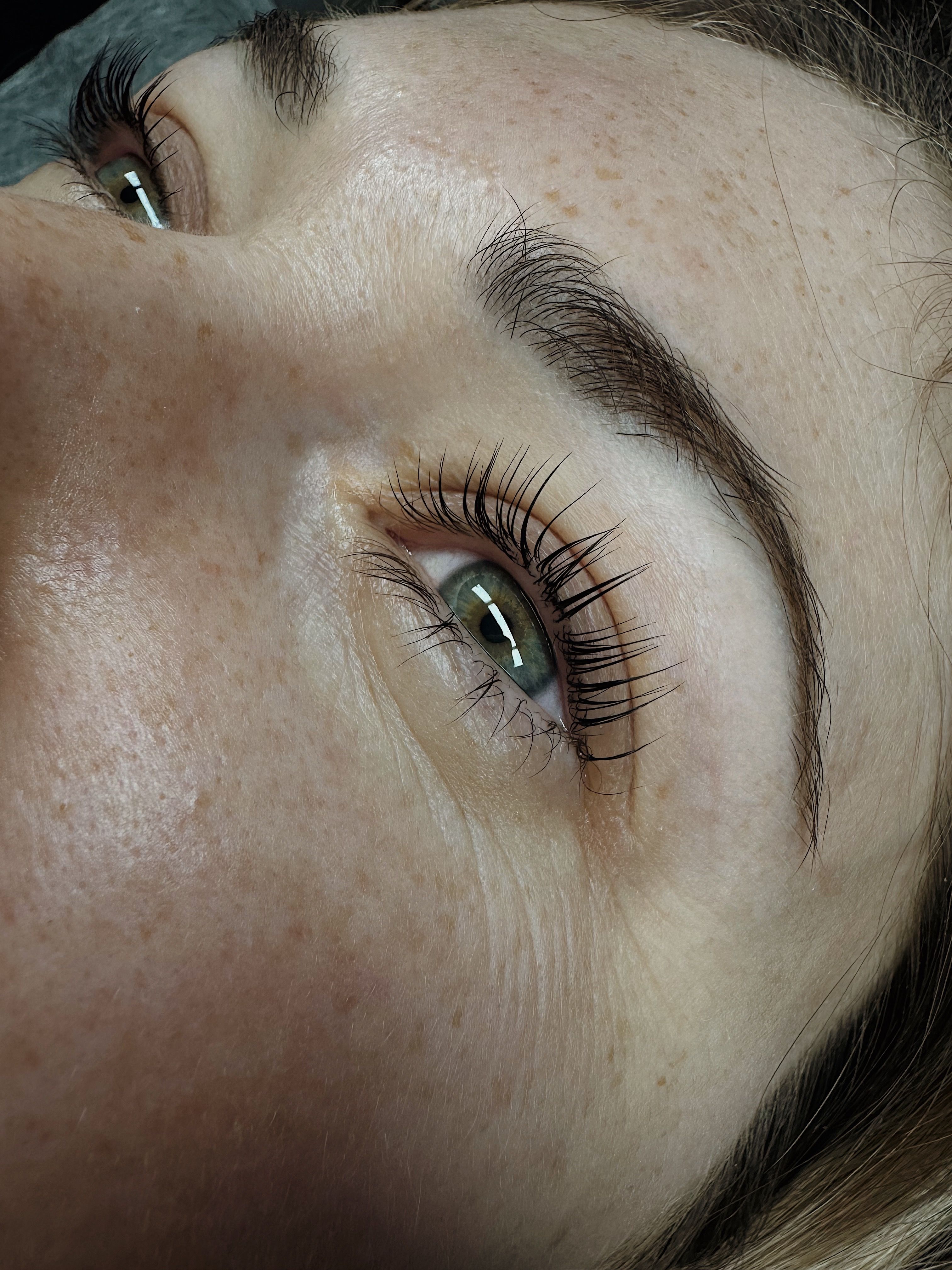 Close-up of a woman's face with long, curled eyelashes and green eyes looking straight 
