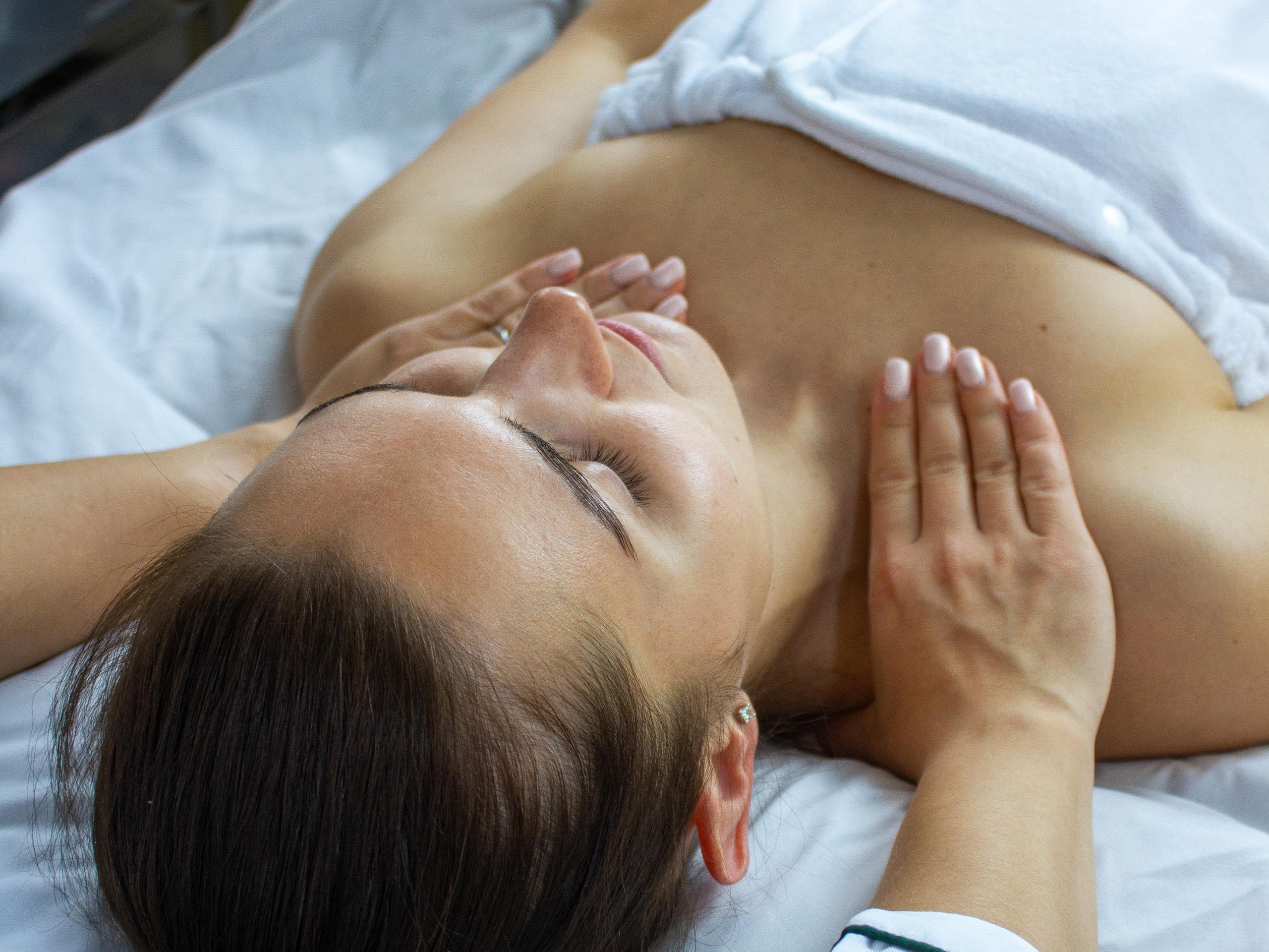 A woman with closed eyes receiving a chest and shoulder massage.