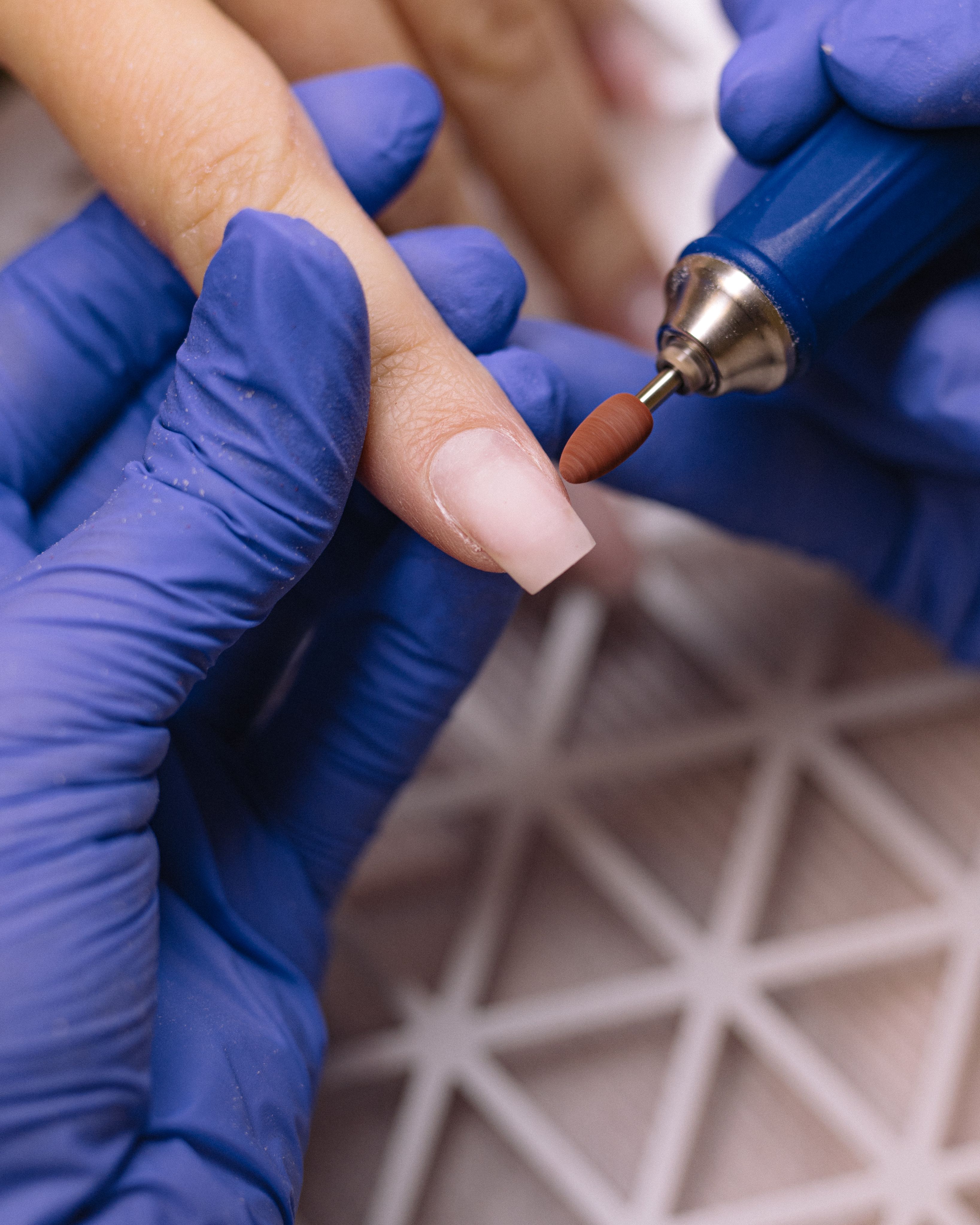 Close-up of a nail technician shaping nails with an electric nail drill