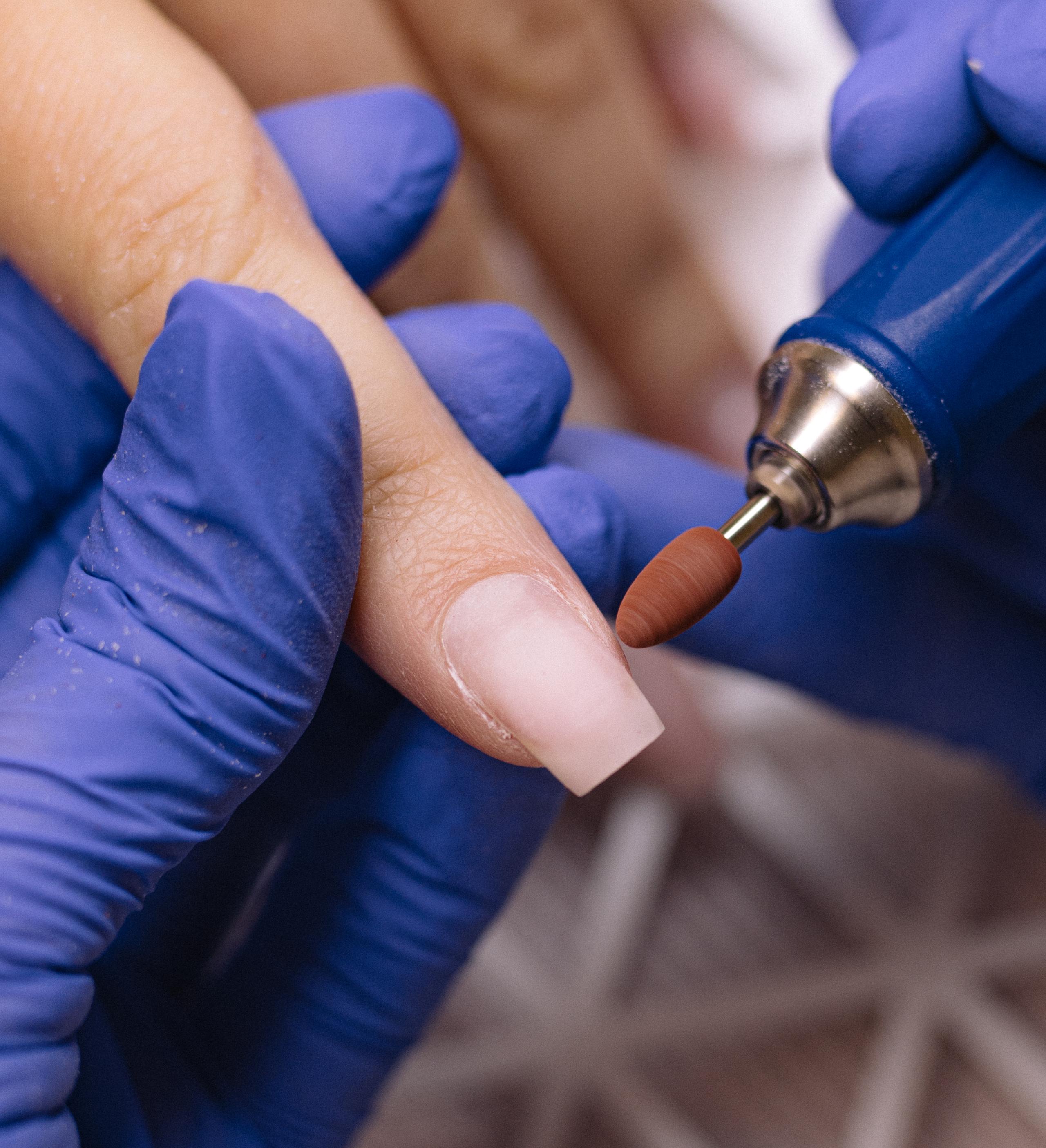 Close-up of a nail technician shaping nails with an electric nail drill
