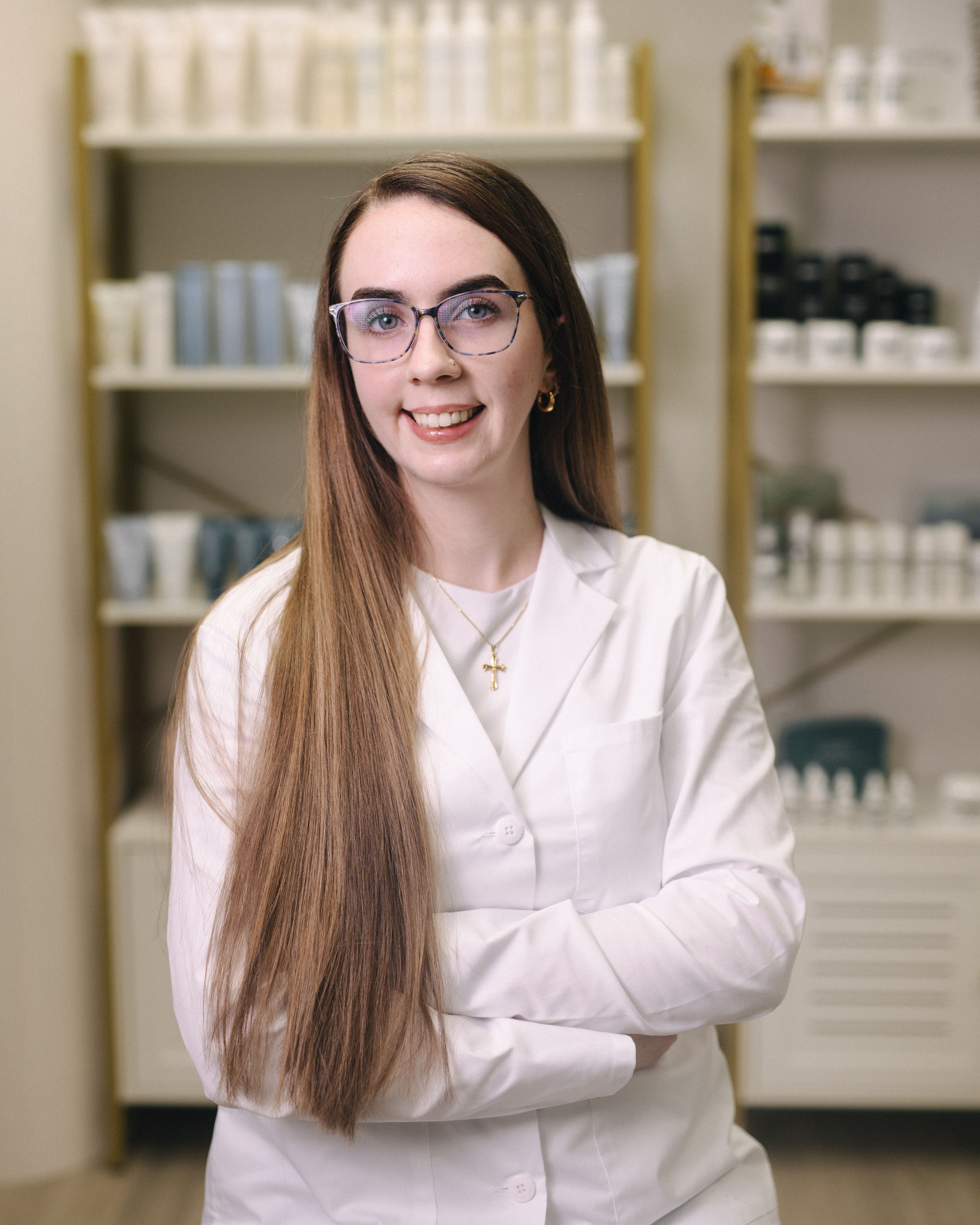 Esthetician in a white coat in a room with product shelves.