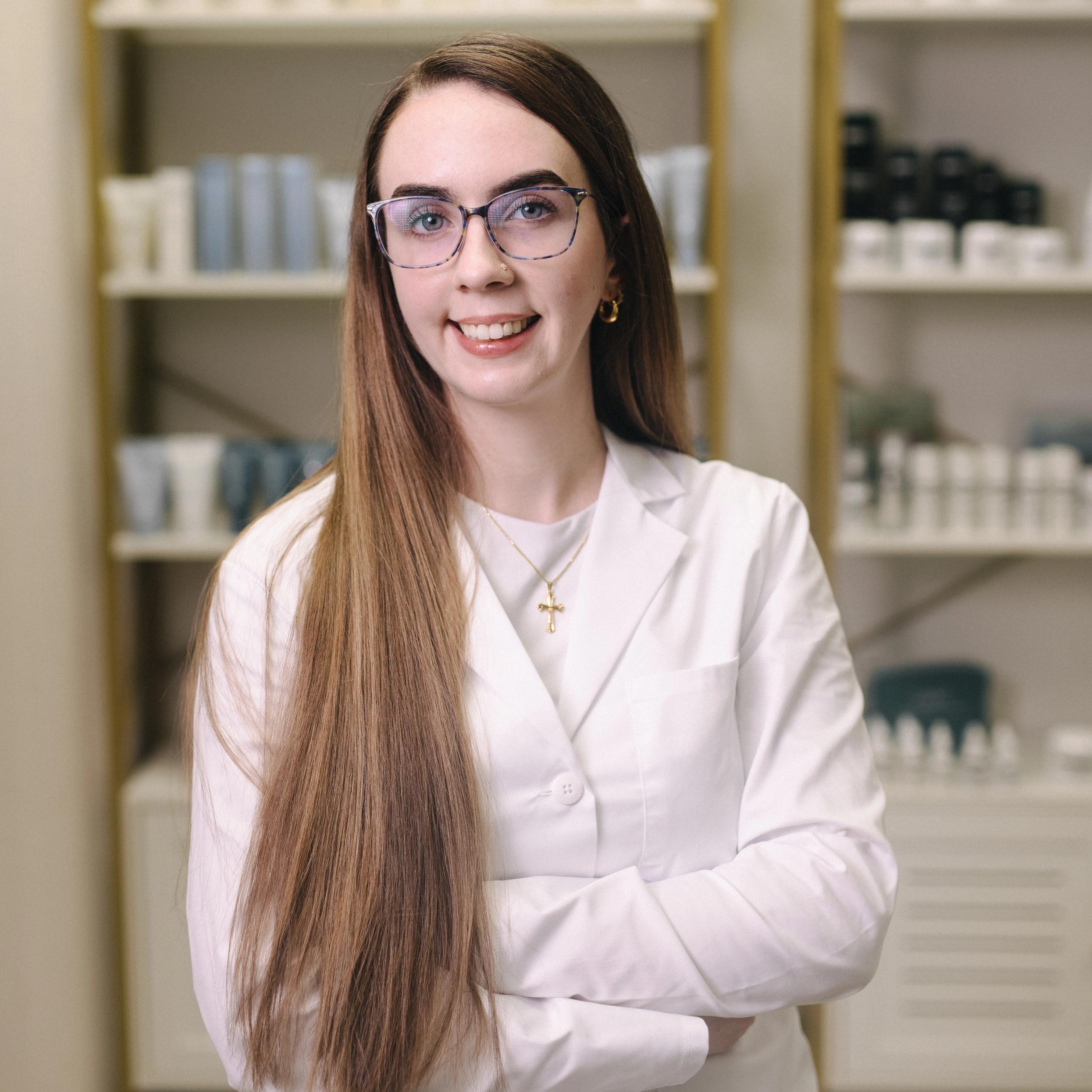 Esthetician in a white coat in a room with product shelves.