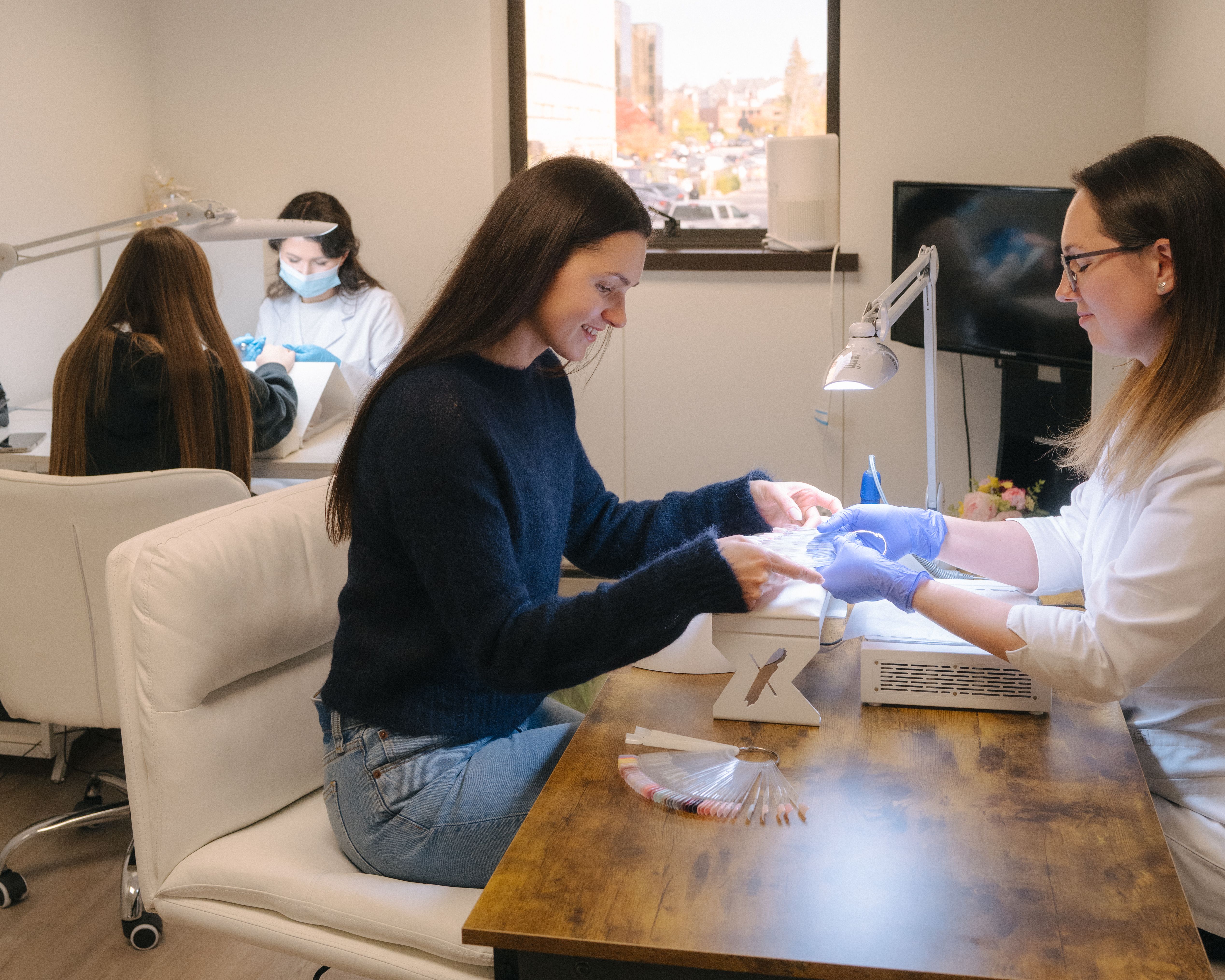 A smiling woman gets a manicure from a technician.
