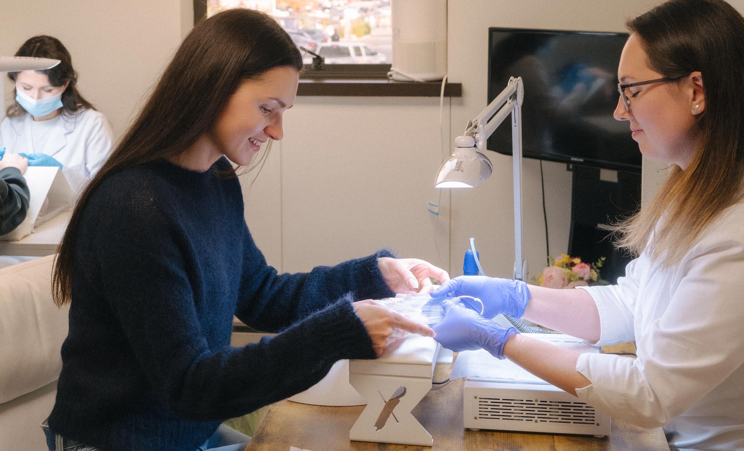 A smiling woman gets a manicure from a technician.
