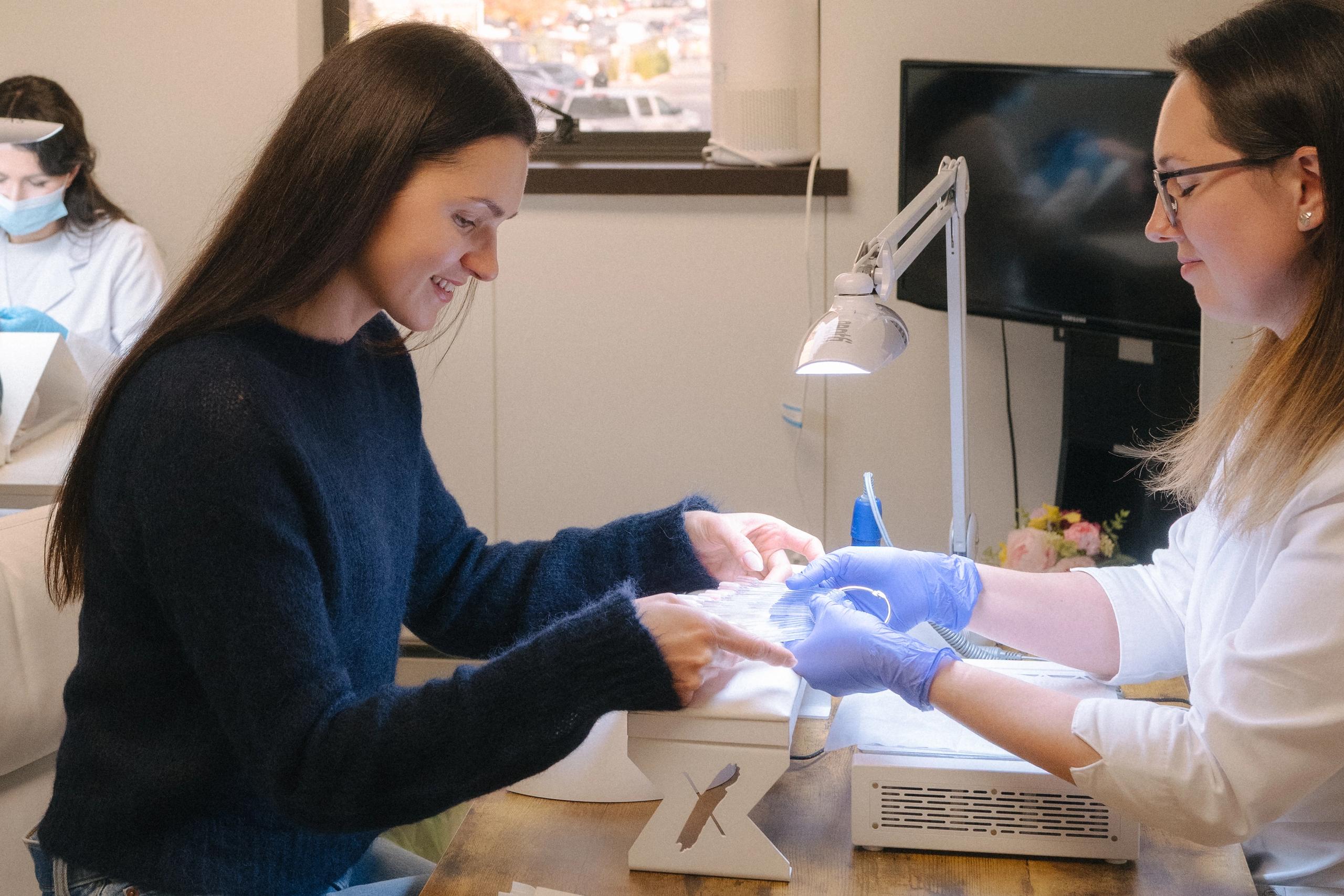 A smiling woman gets a manicure from a technician.