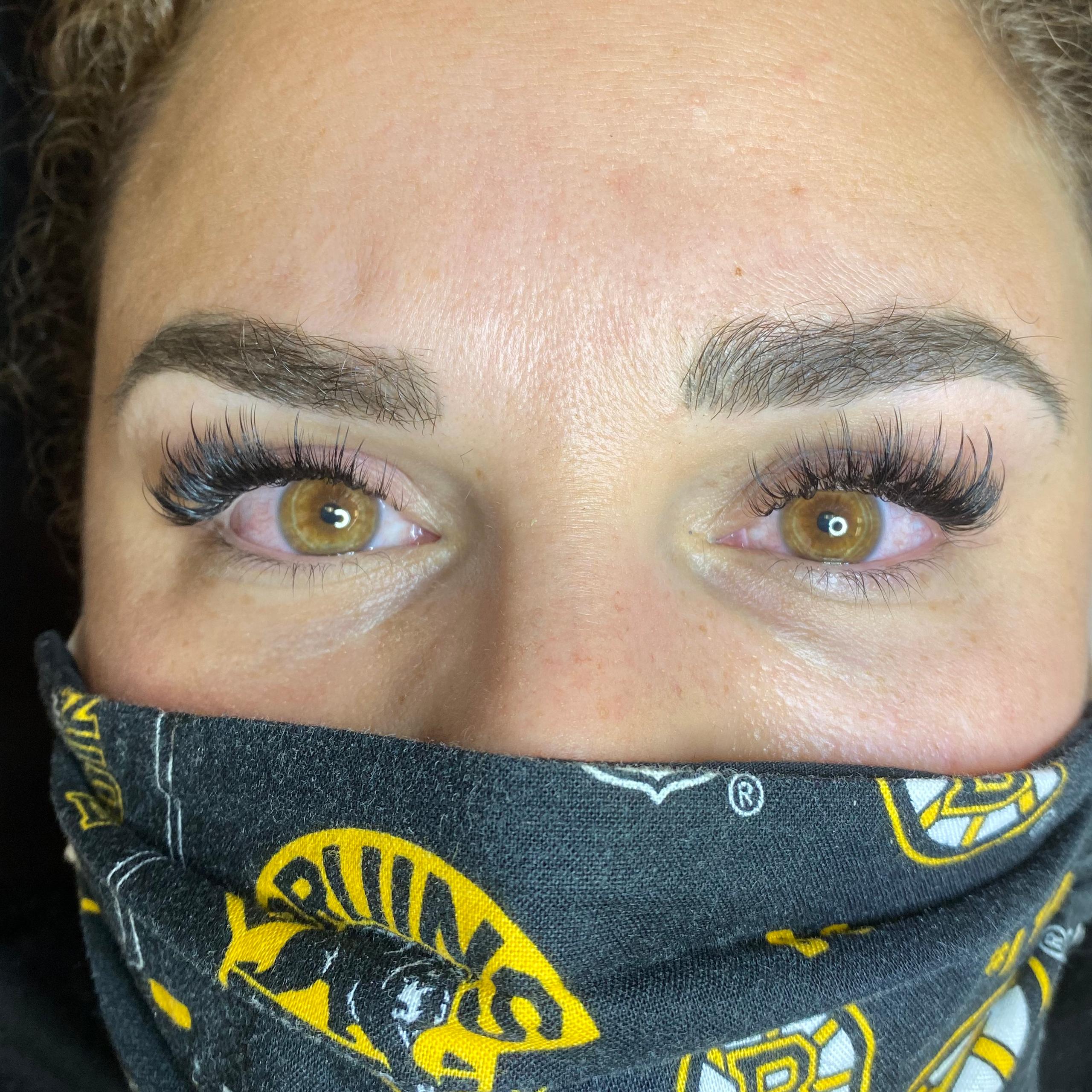 A person's face with full, dark eyelashes, defined eyebrows, and wearing a black face mask.