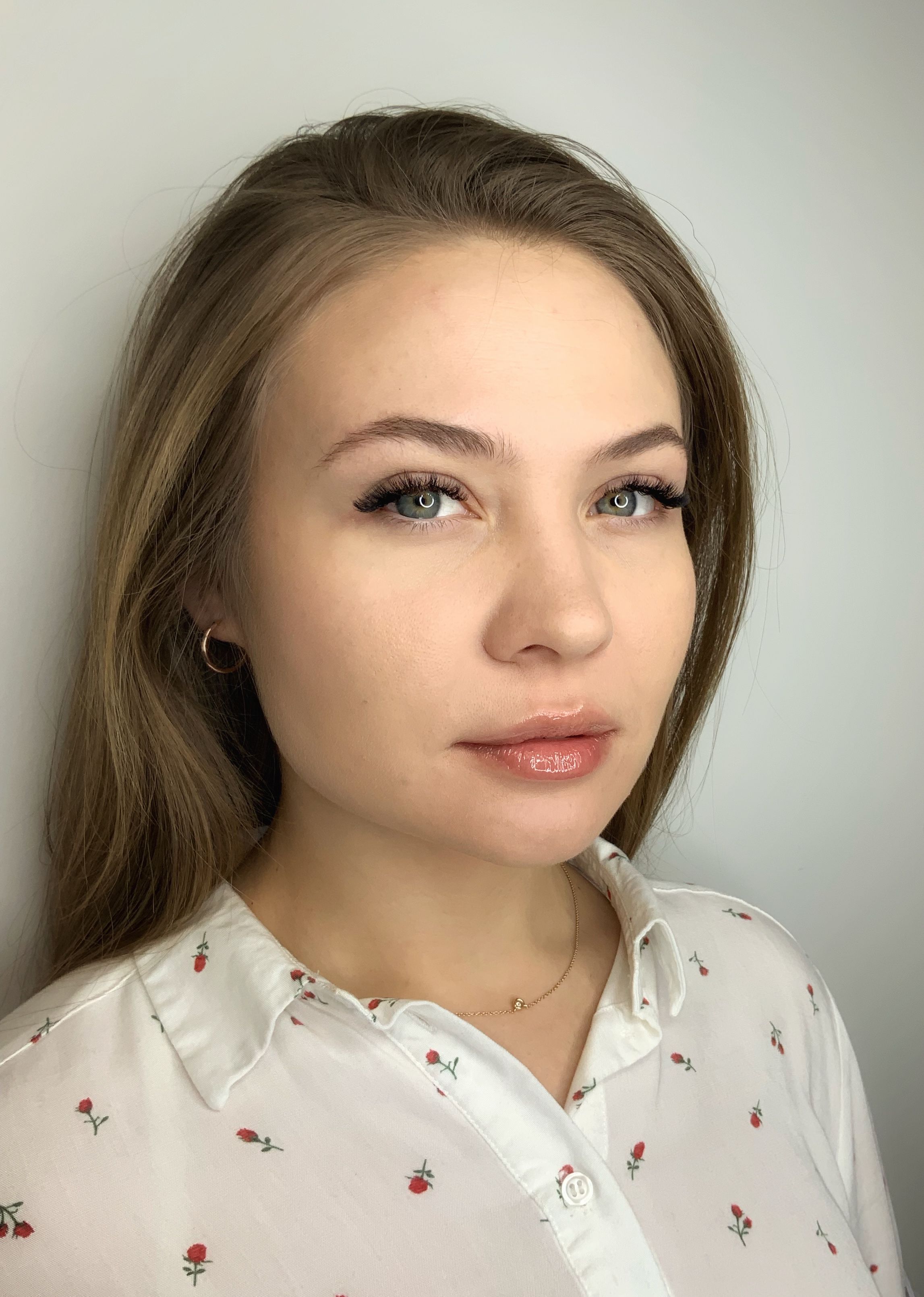 A portrait of a woman with long brown hair, light eyes, long eyelashes, and glossy lips.