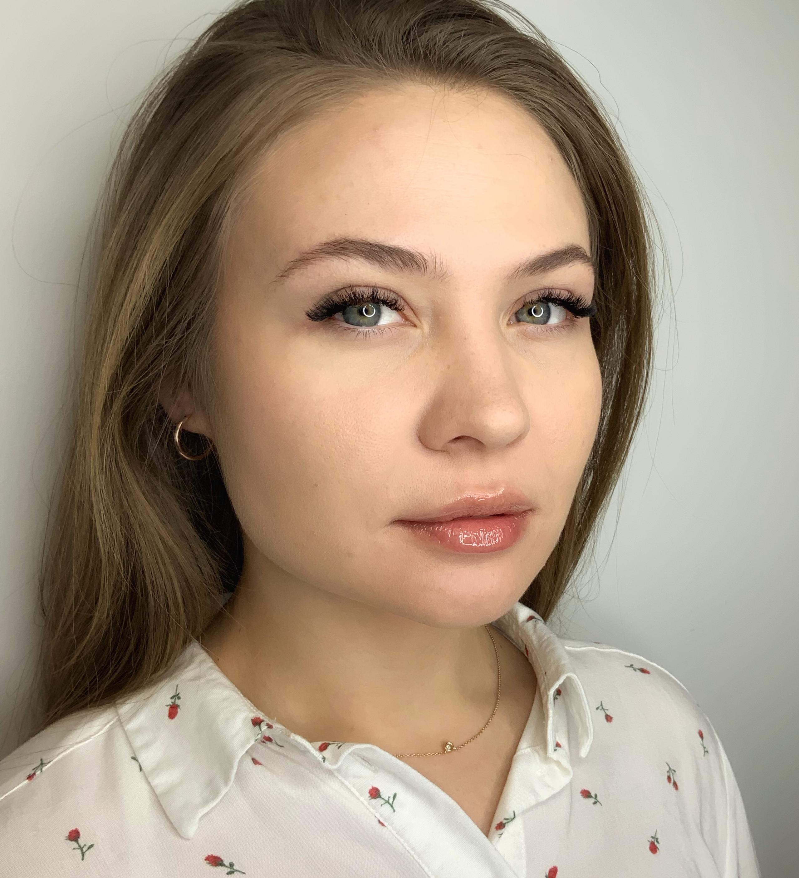 A portrait of a woman with long brown hair, light eyes, long eyelashes, and glossy lips.