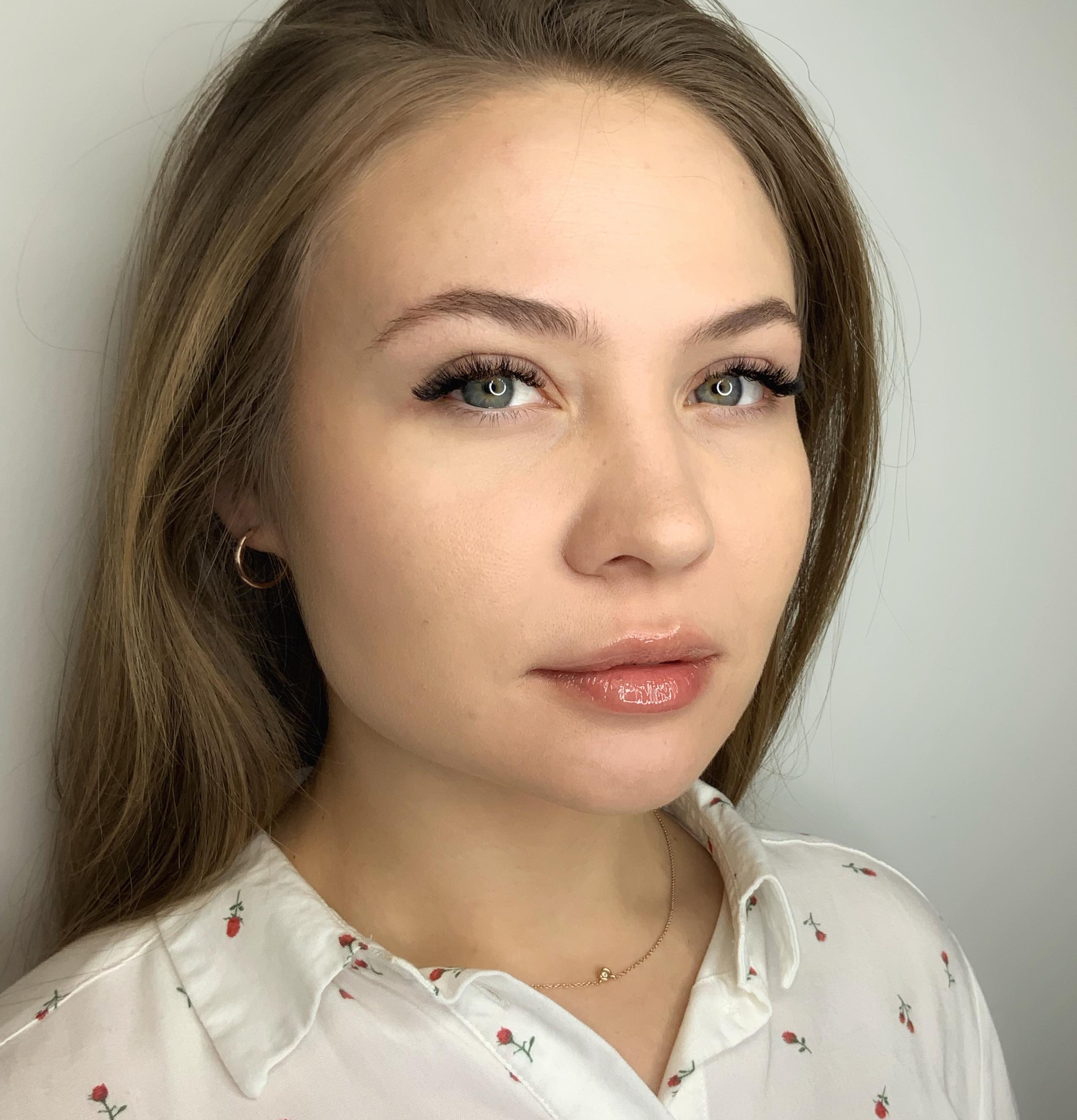 A portrait of a woman with long brown hair, light eyes, long eyelashes, and glossy lips.