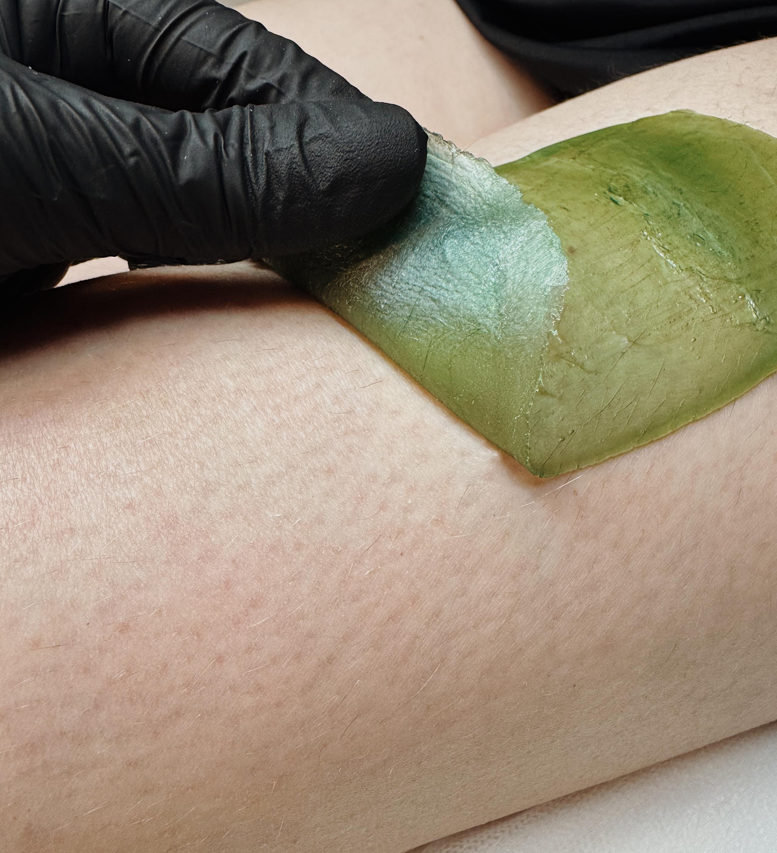 A hand in a glove holds wax on a leg