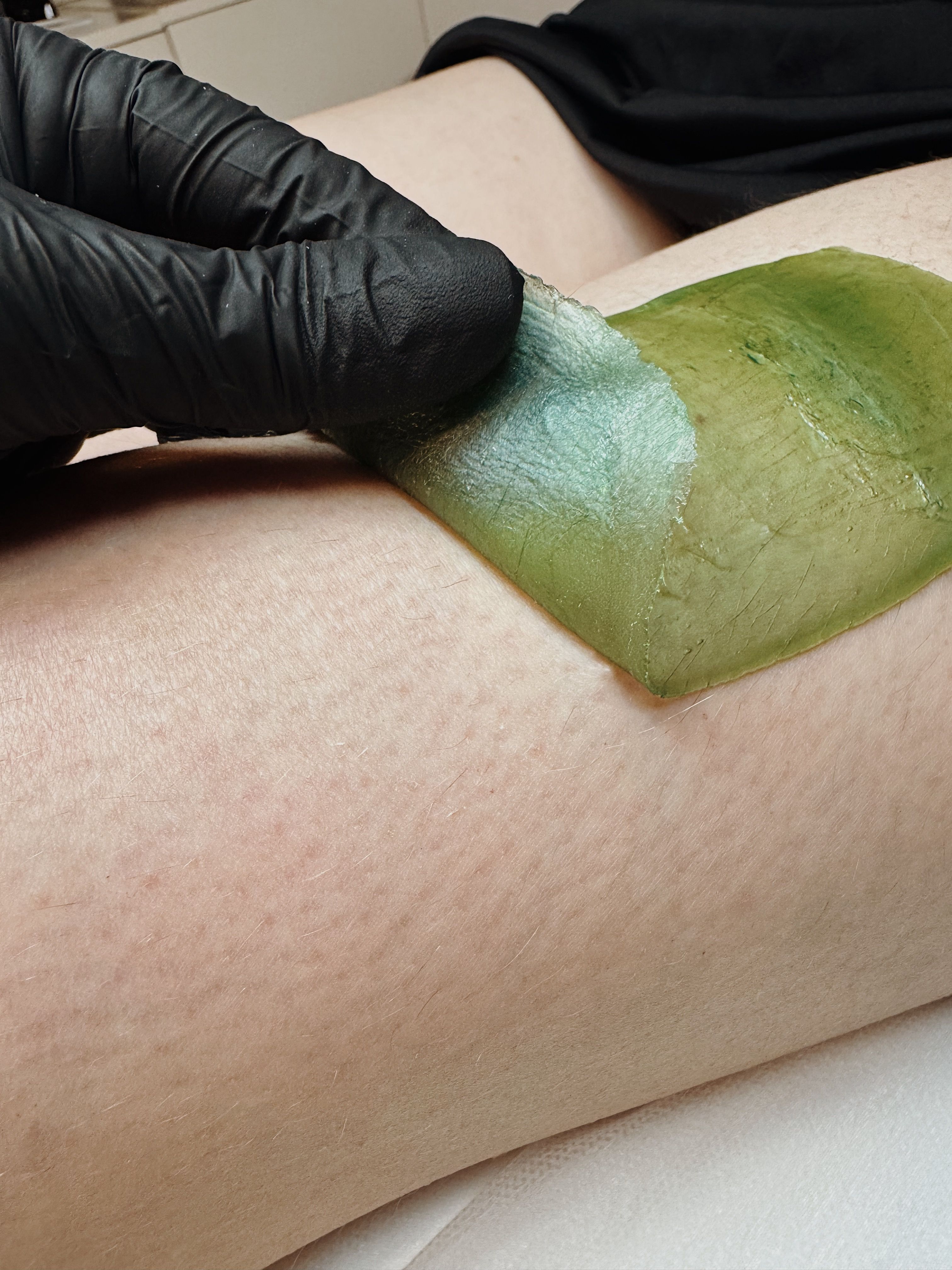 green wax on a girl's leg and a hand in a black mitten