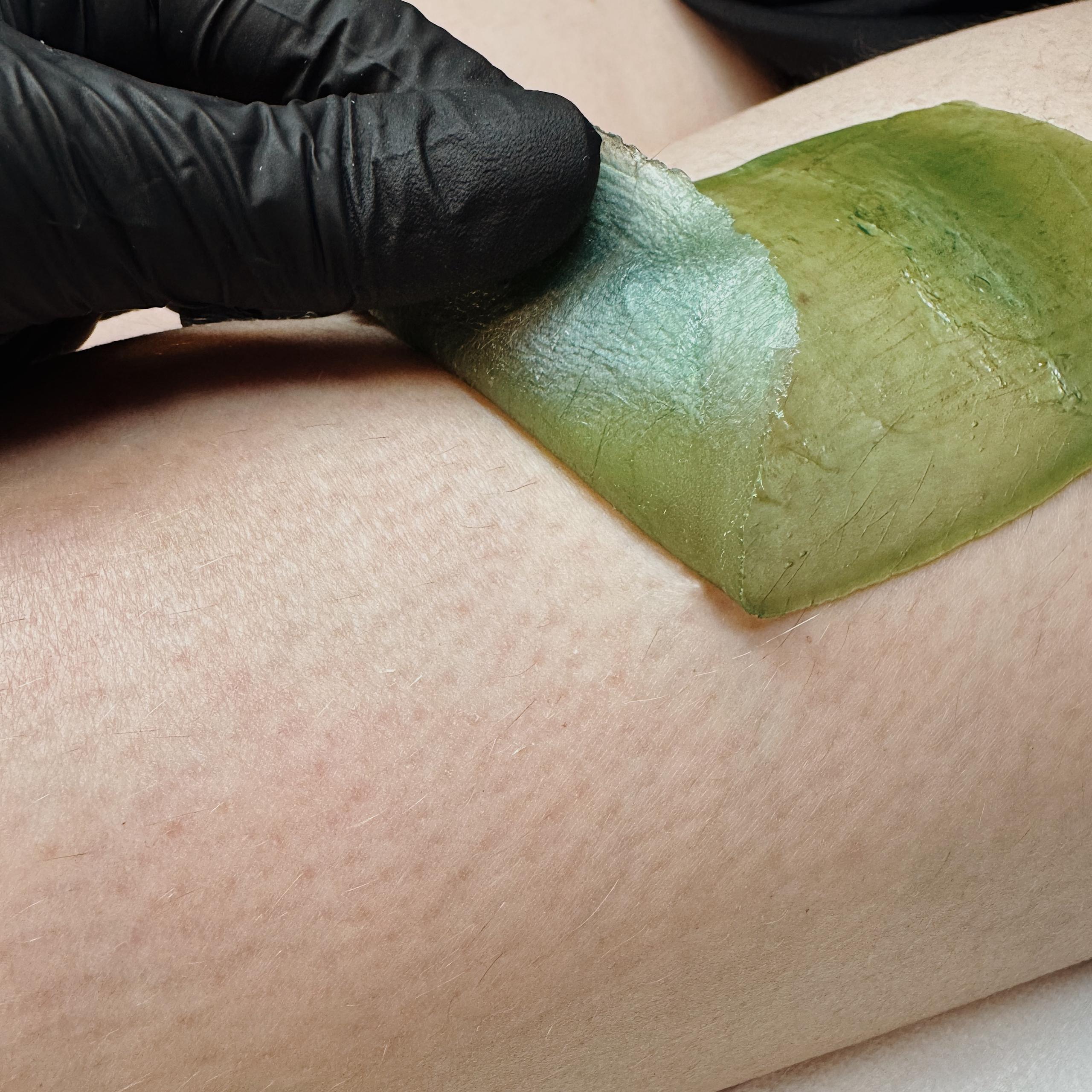 green wax on a girl's leg and a hand in a black mitten