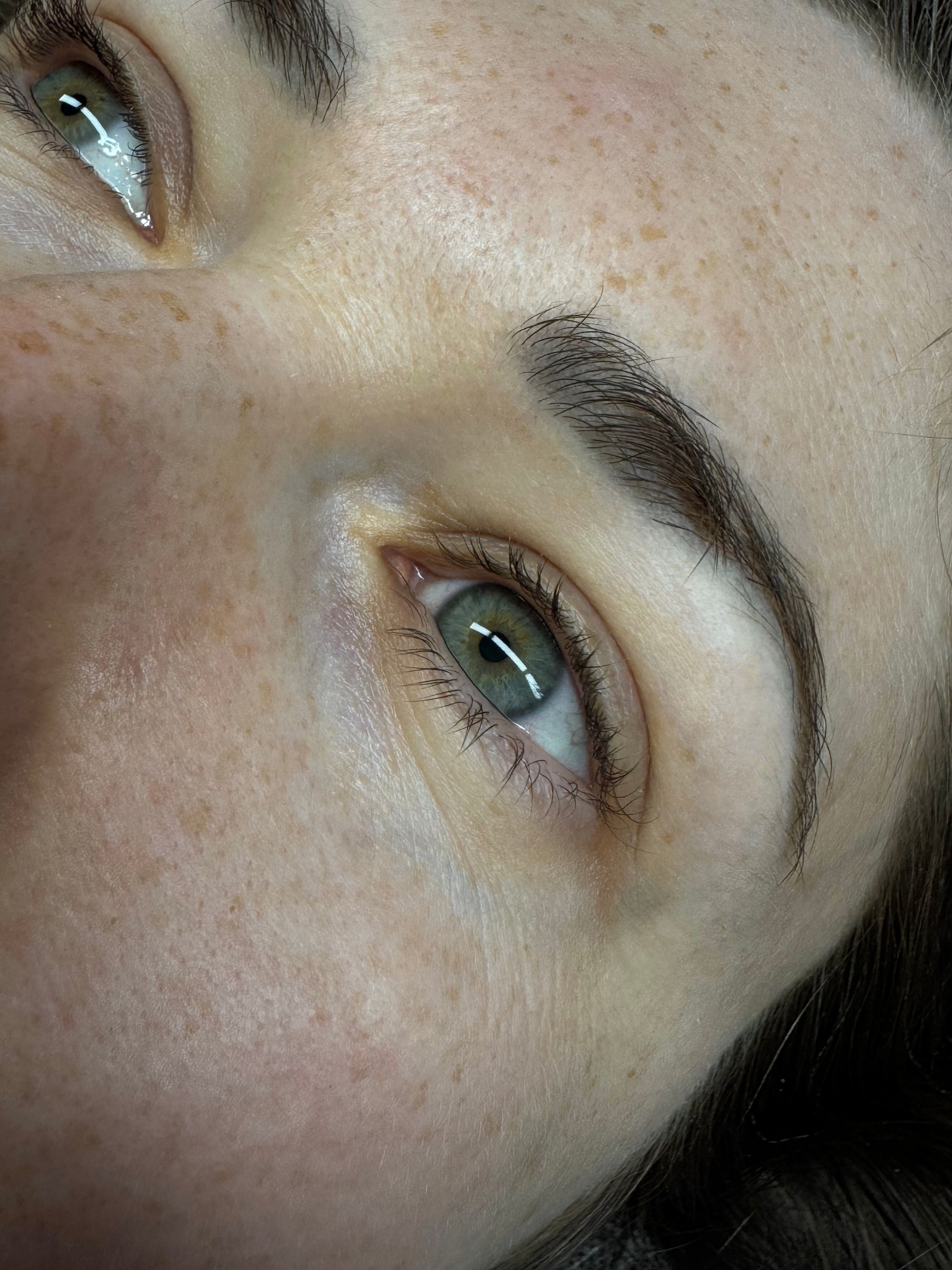 Close-up of a person's two green-grey eyes and brown eyebrows.