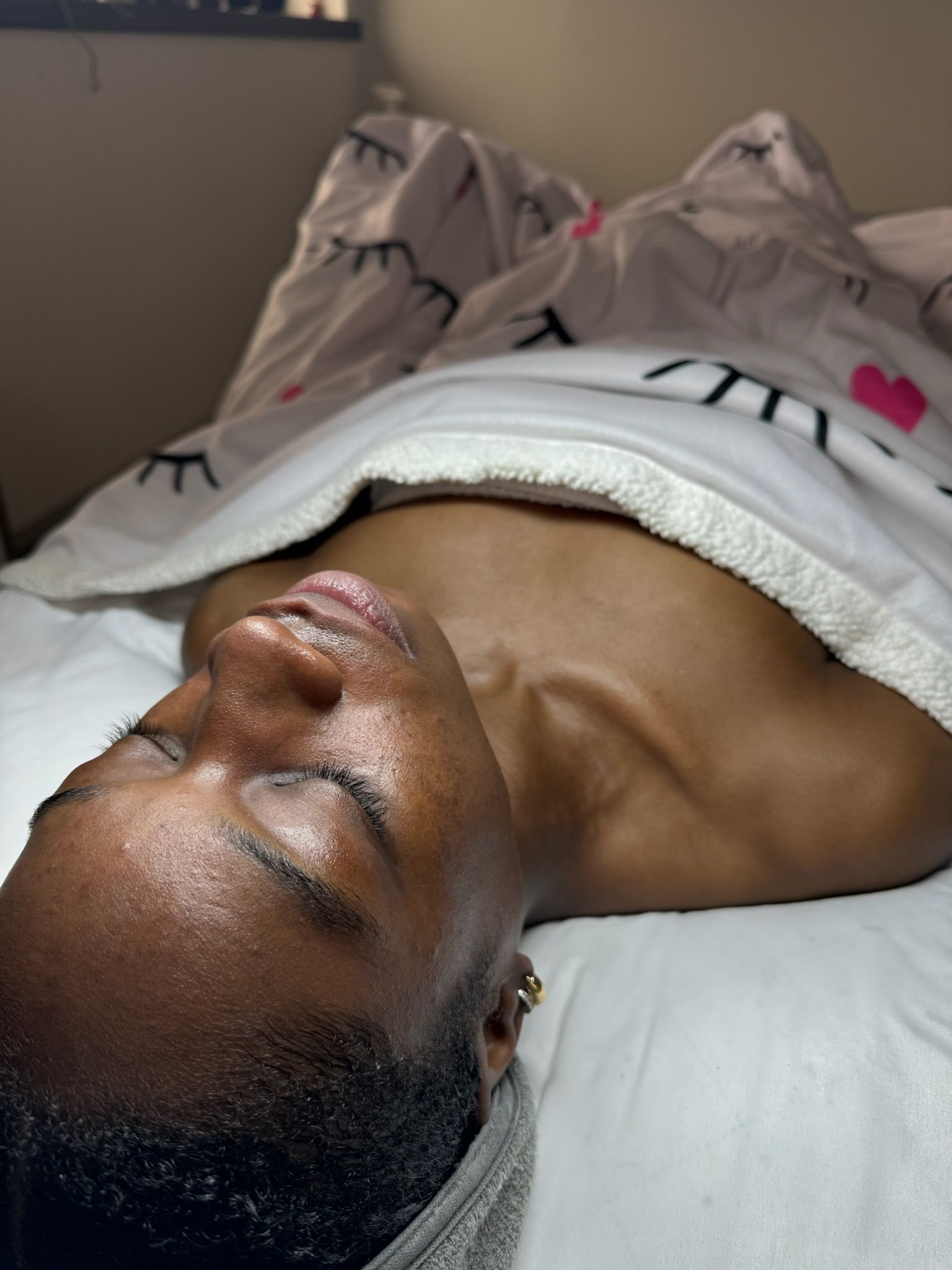 A person lies down with eyes closed, covered by a white blanket.