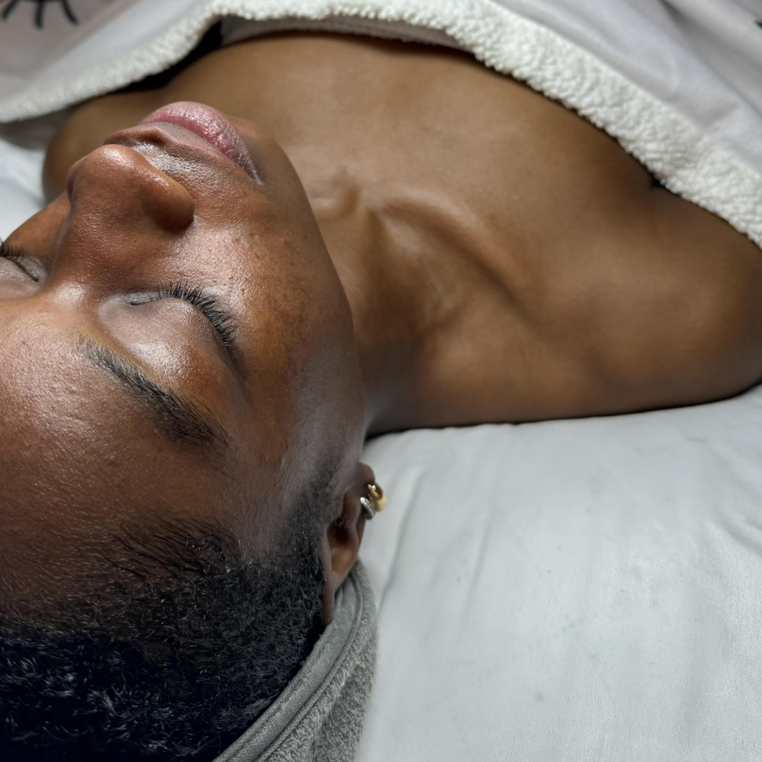 A person lies down with eyes closed, covered by a white blanket.