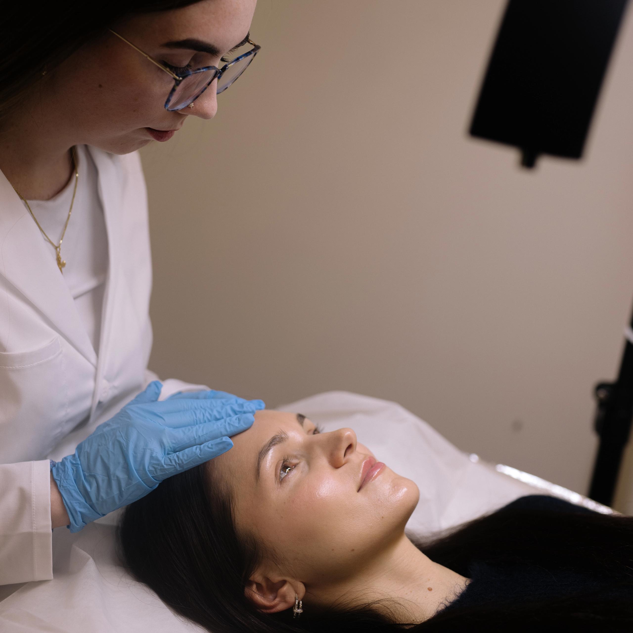 A technician in blue gloves gently touches a woman's forehead