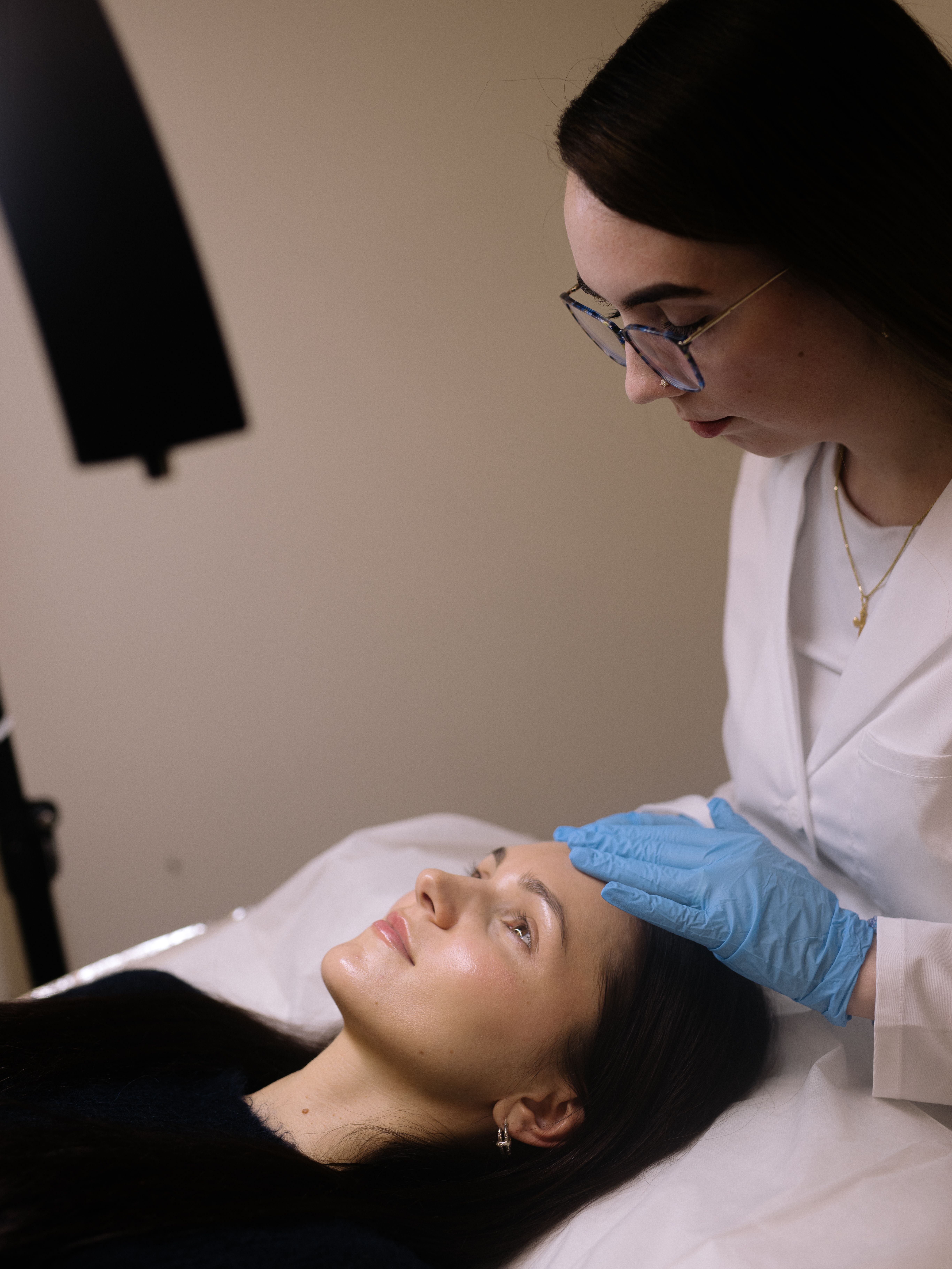 An esthetician in blue gloves performs a skincare treatment on a client.