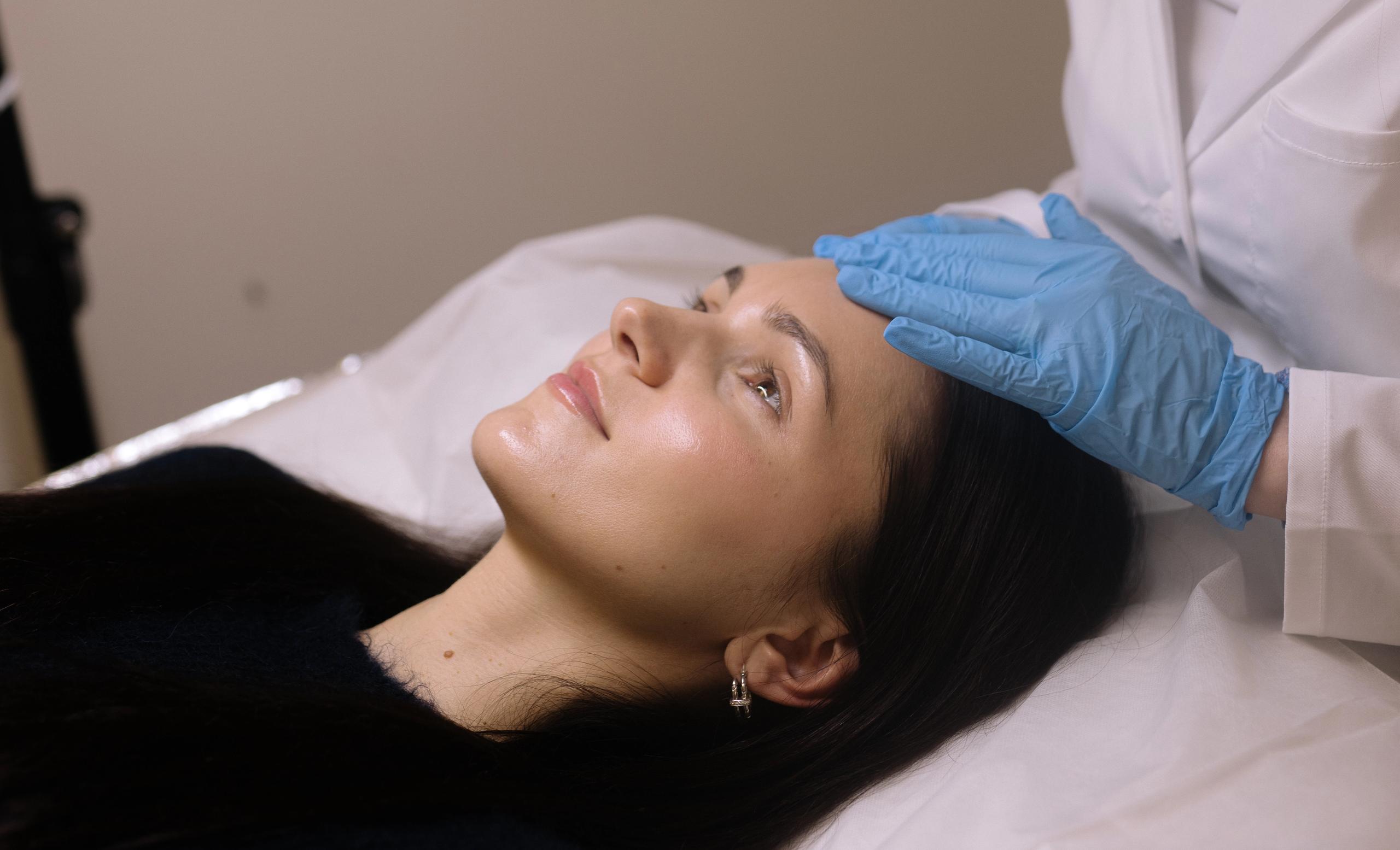An esthetician in blue gloves performs a skincare treatment on a client.