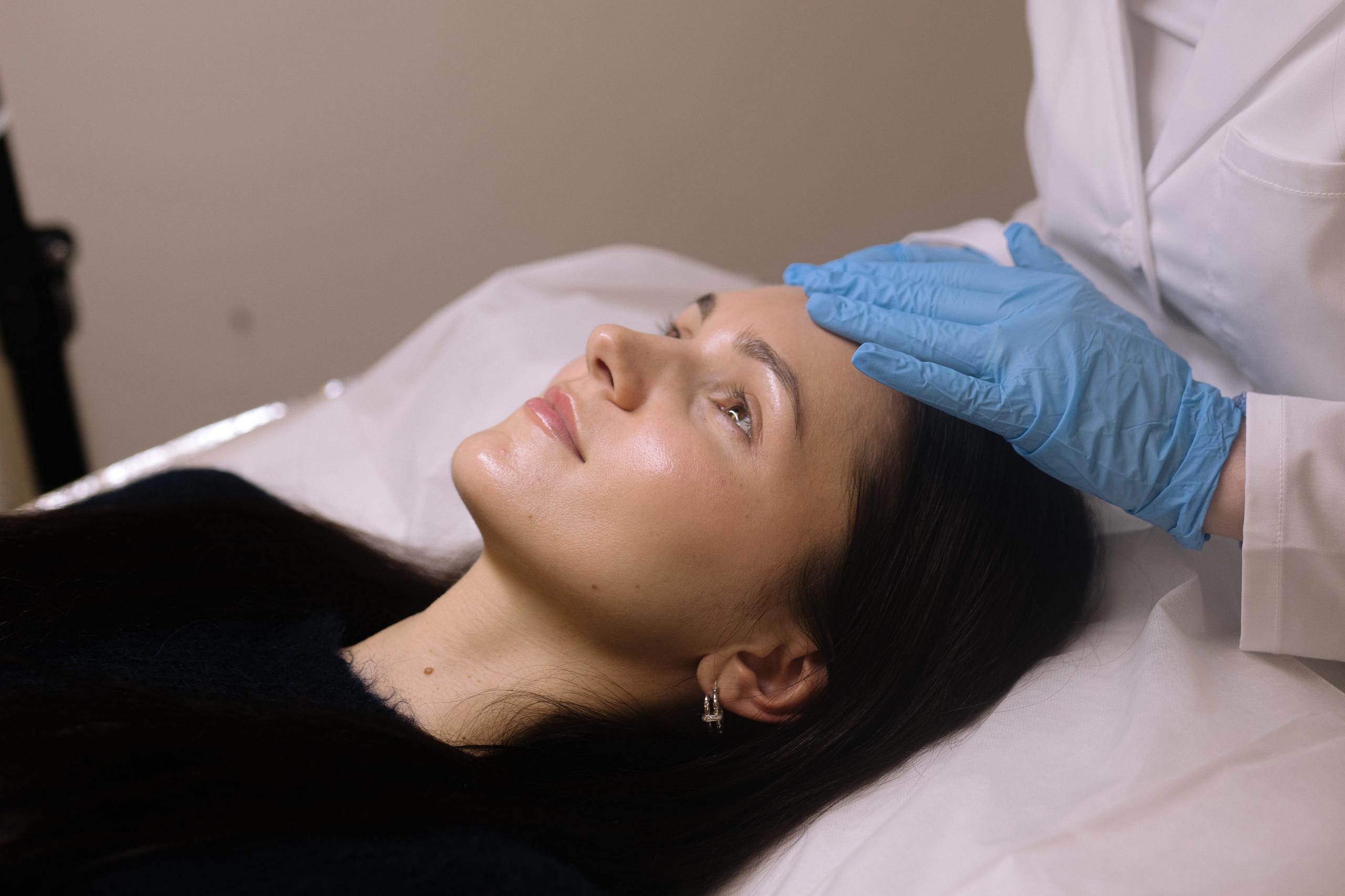 An esthetician in blue gloves performs a skincare treatment on a client.