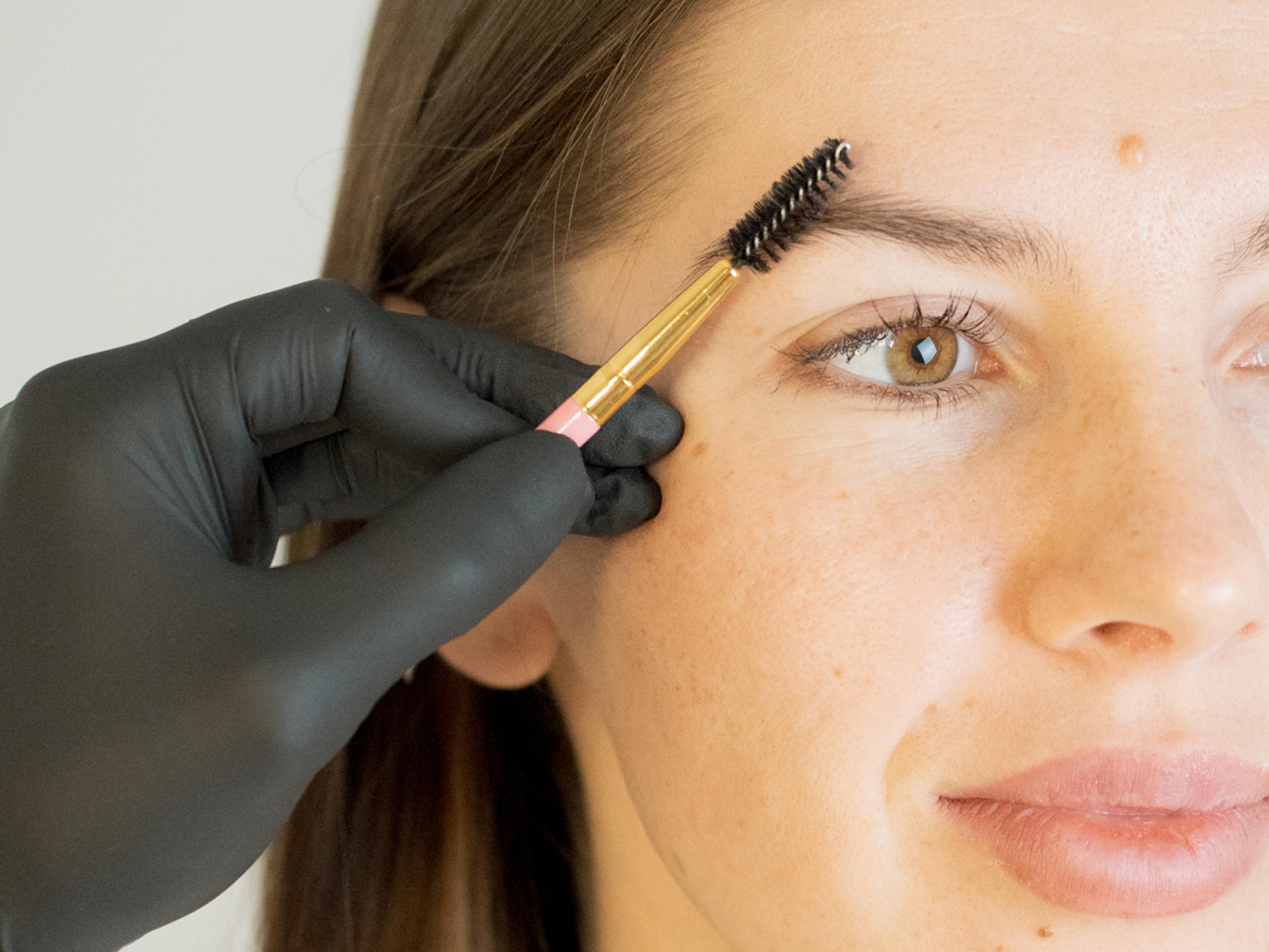 Esthetician brushes a client's freshly tinted eyebrow with a spoolie.