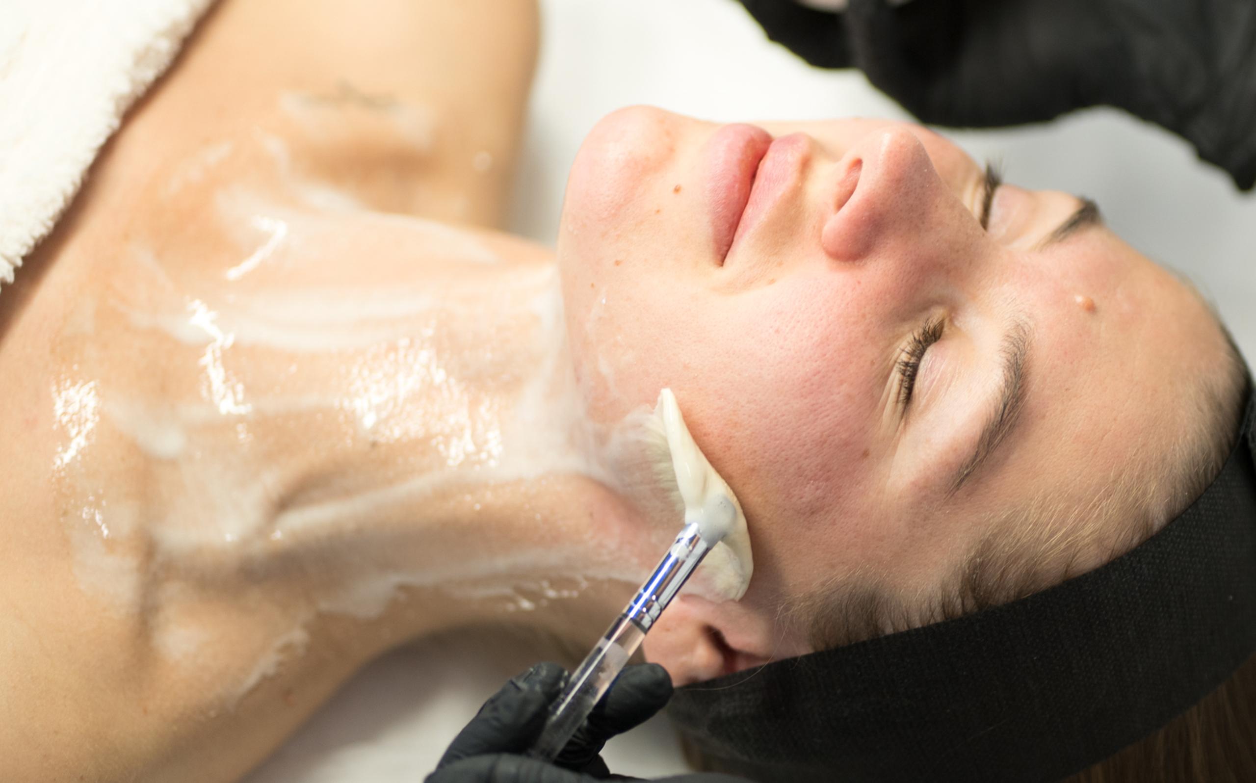Aesthetician applying a creamy mask to a client's face and neck.
