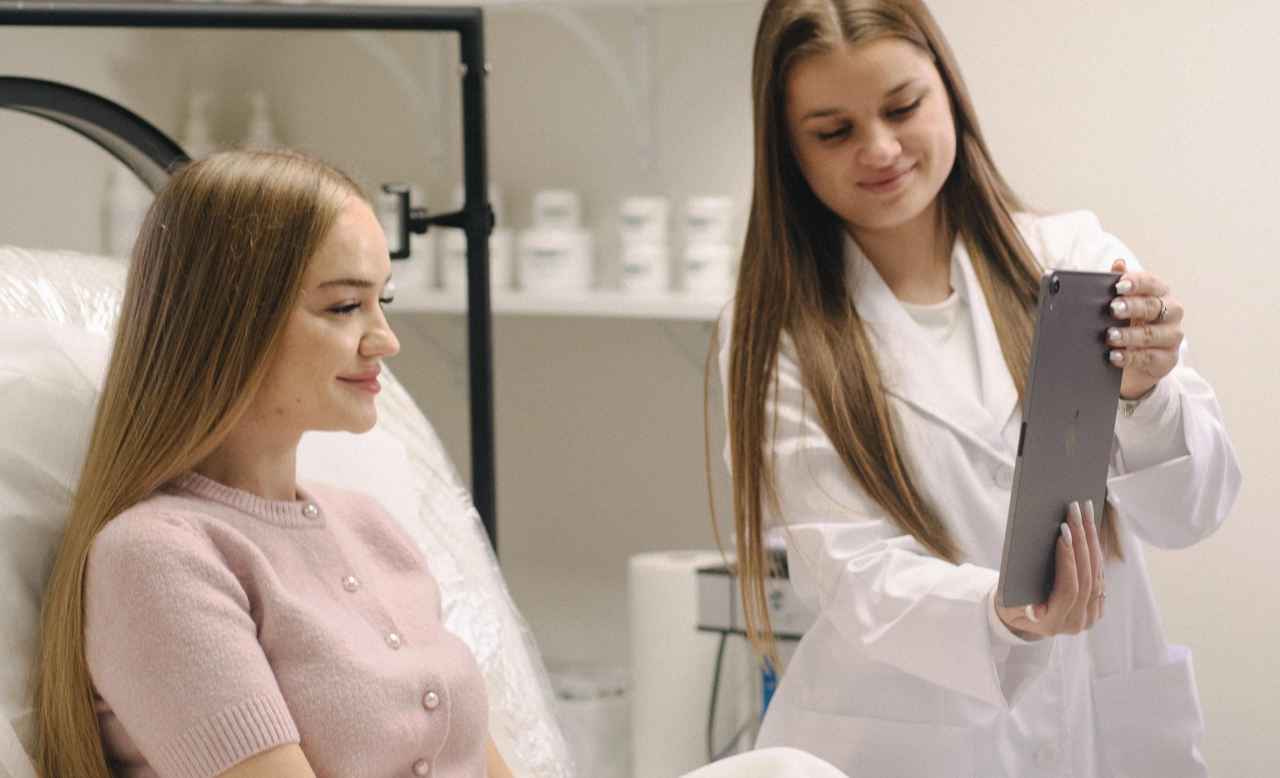 A professional in a lab coat shows a tablet to a smiling client.