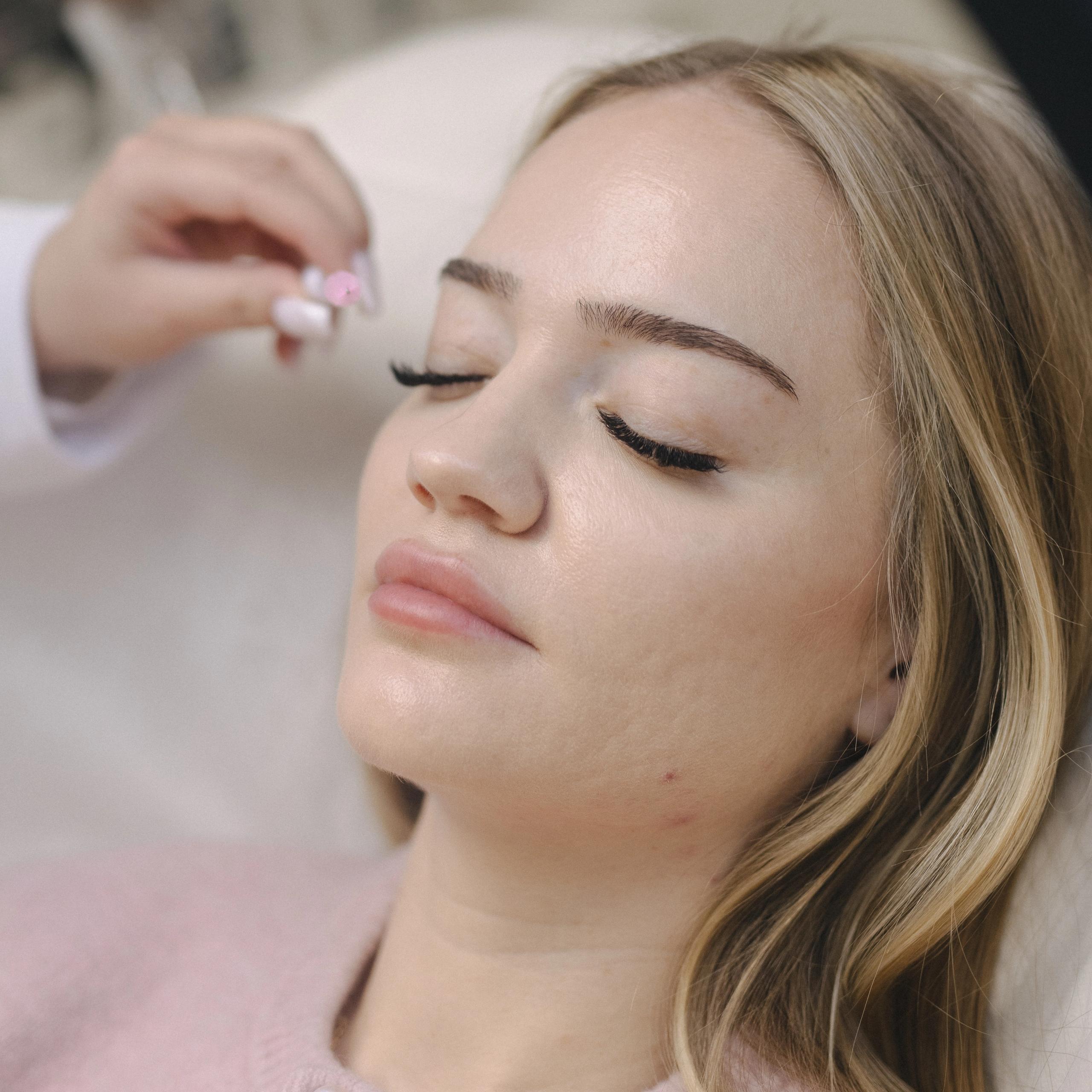 A blonde woman with closed eyes receives a lash treatment.