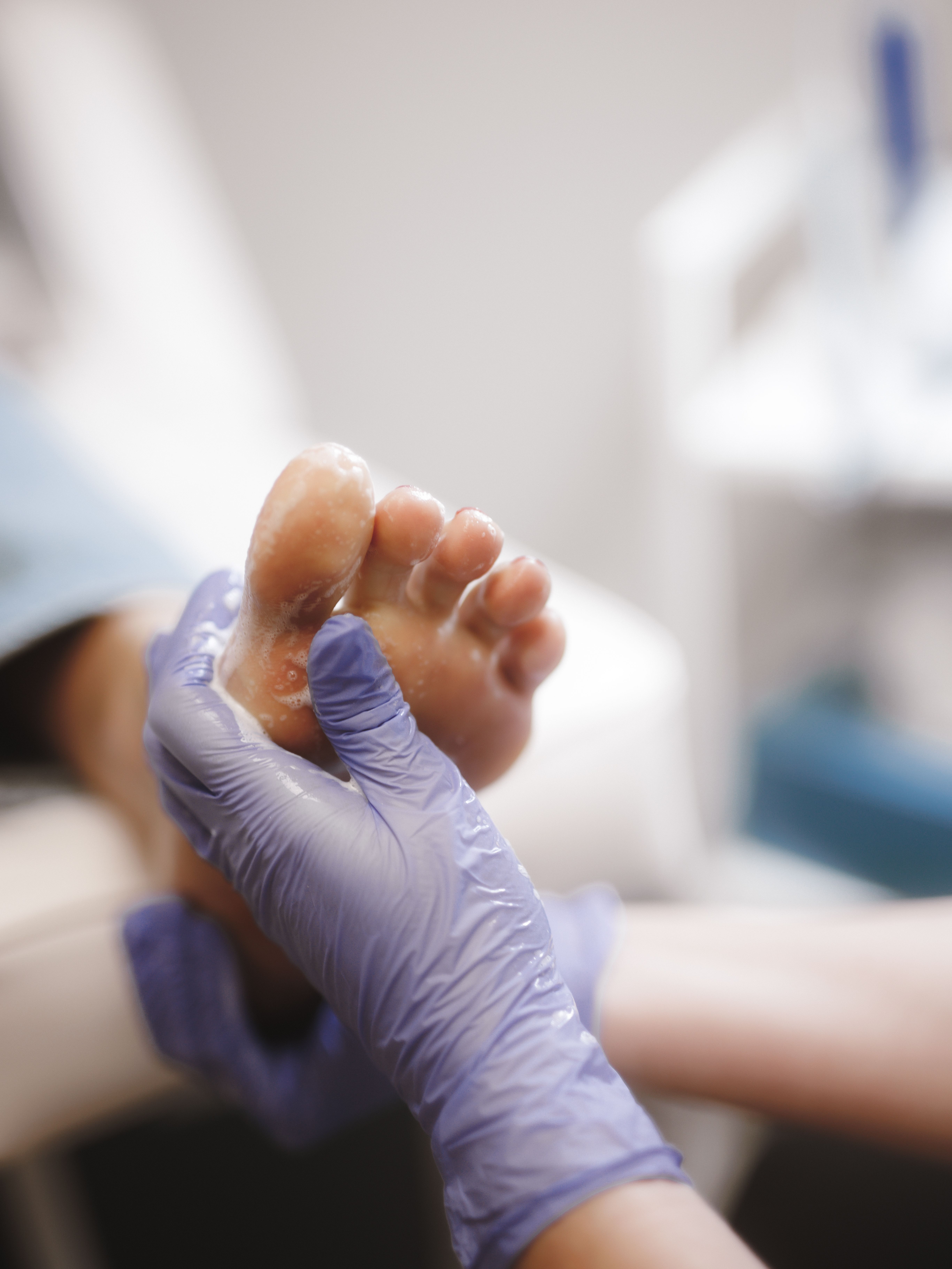 A gloved hand scrubbing a foot with a foamy product.