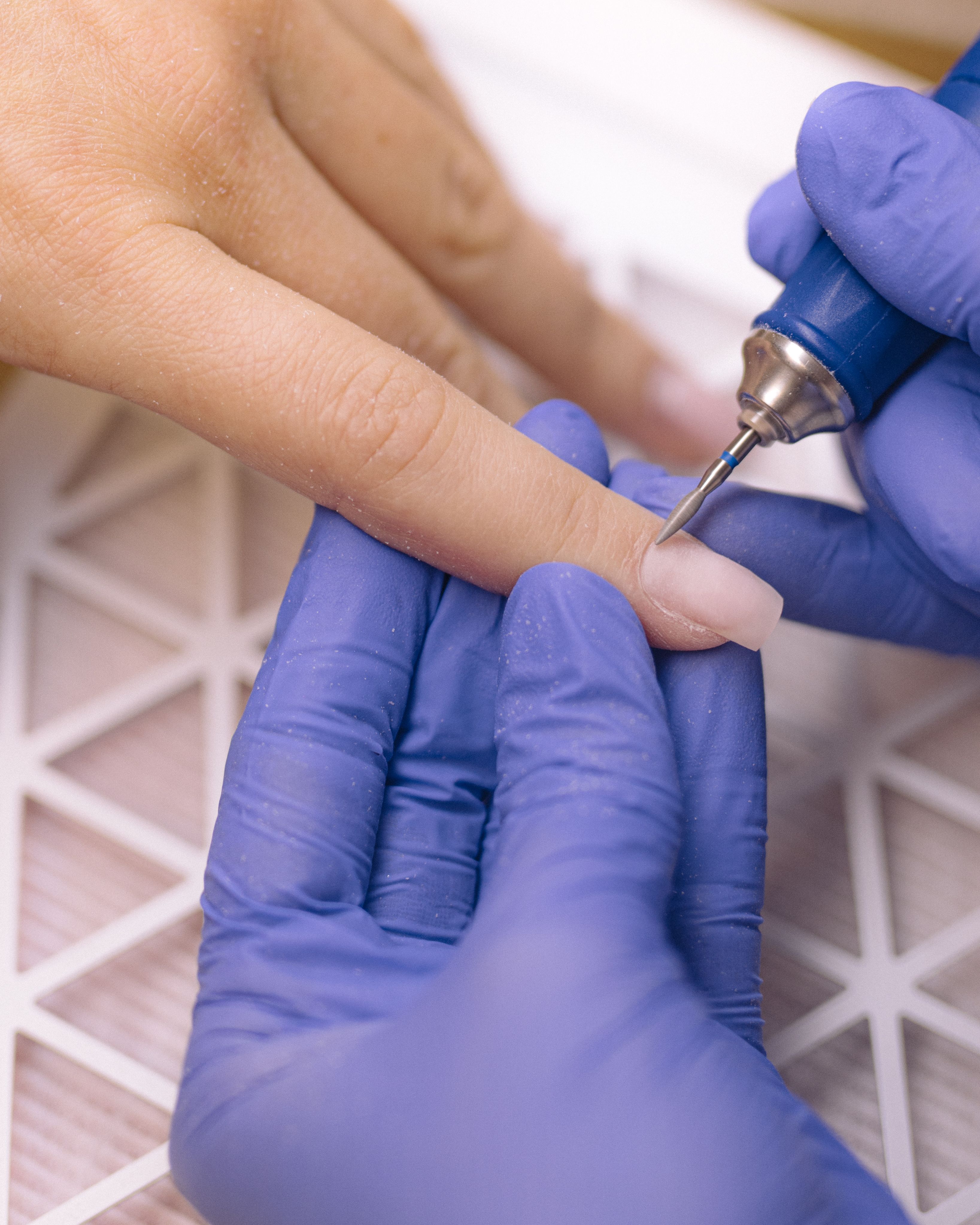 A gloved hand uses an electric nail file to shape an artificial nail.
