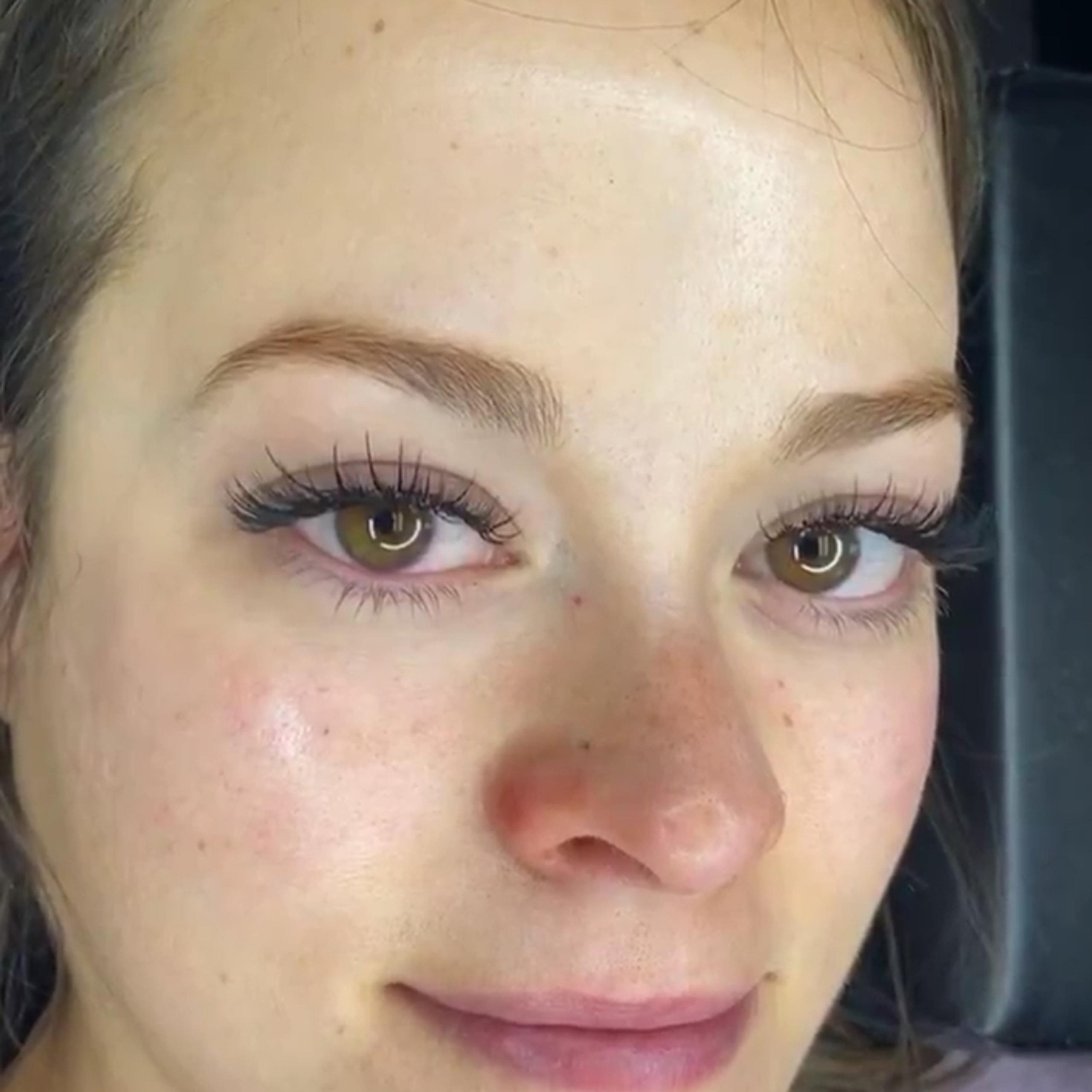 A woman with brown eyes and long, dark eyelashes smiles slightly.