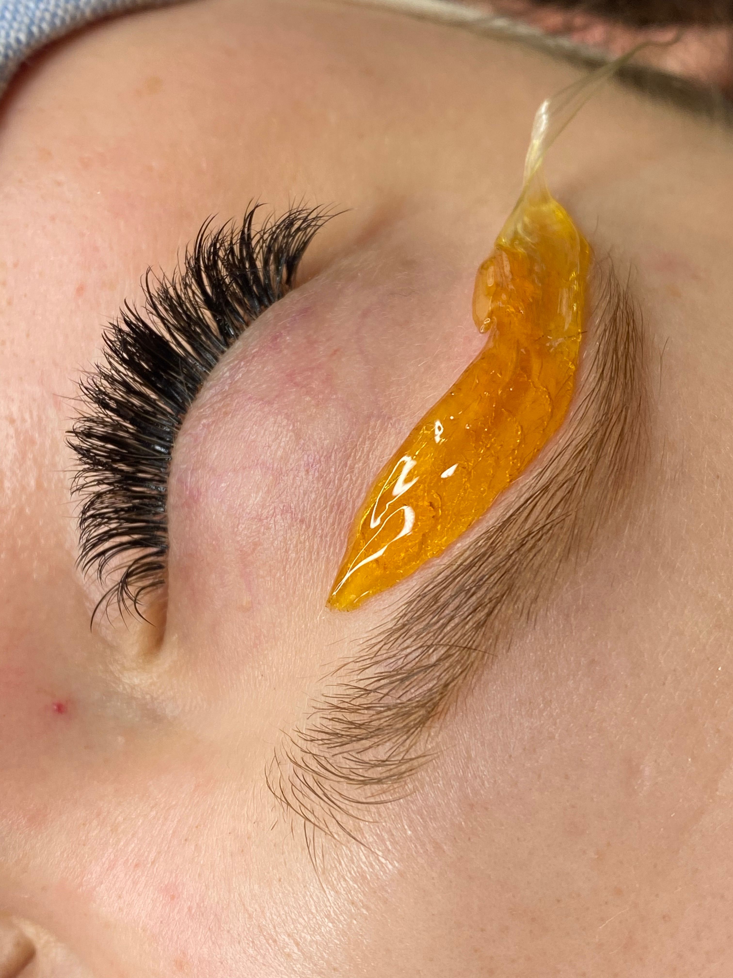Close-up of an eye with thick eyelashes and a golden wax strip on the eyebrow.