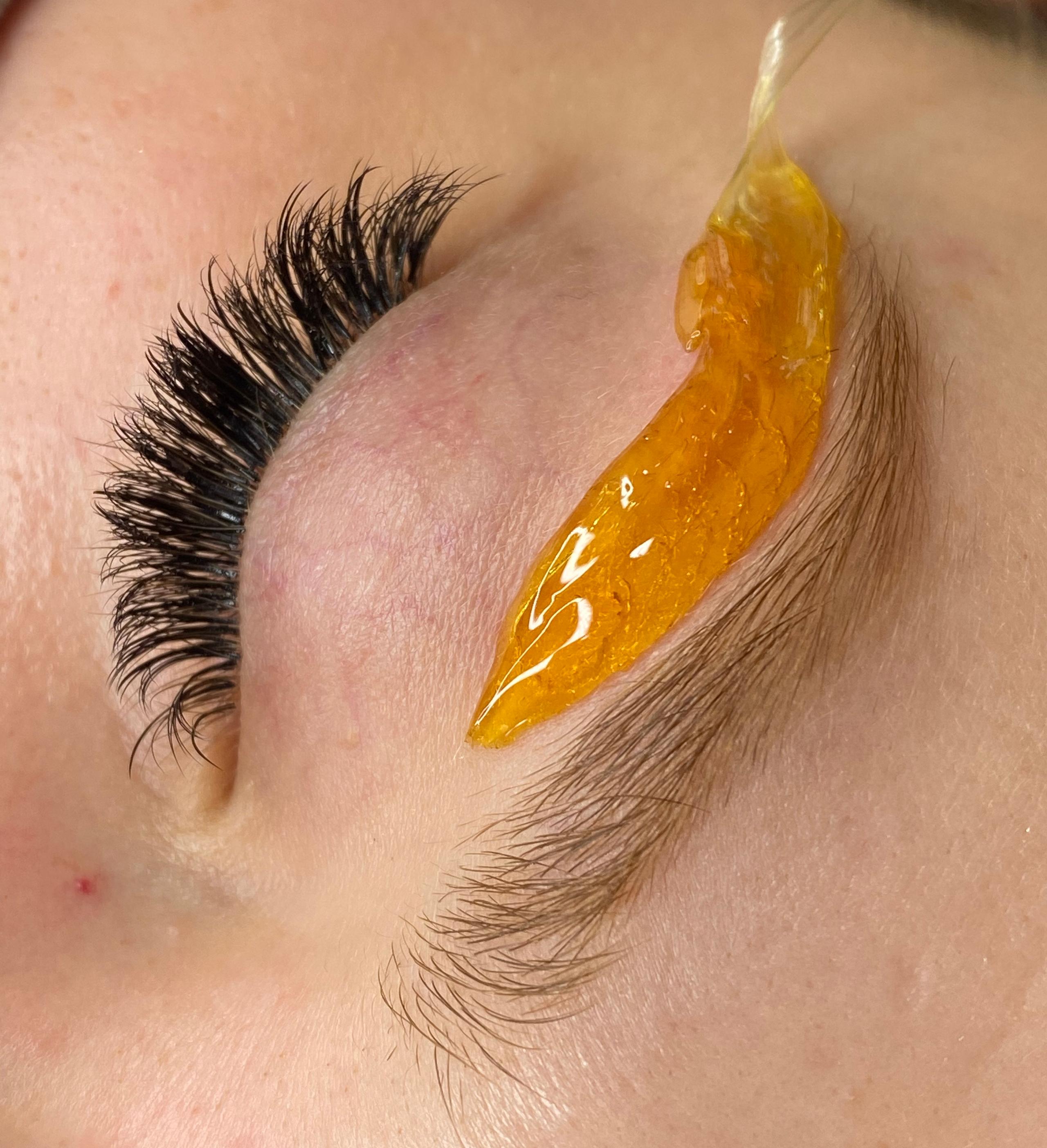 Close-up of golden wax applied beneath a client's eyebrow.