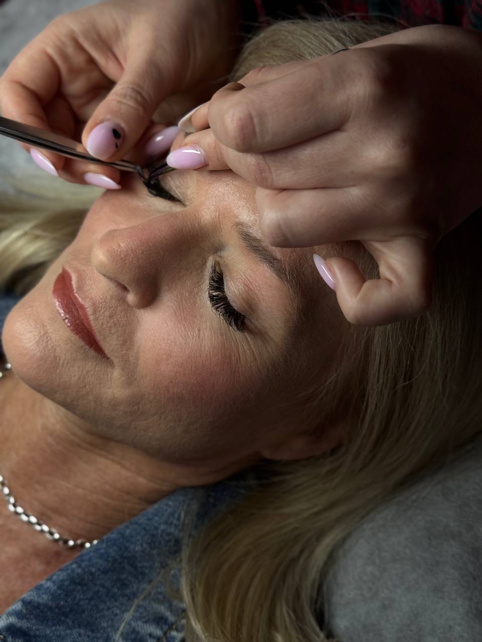 Close-up of an esthetician applying eyelash extensions to a woman's eye.