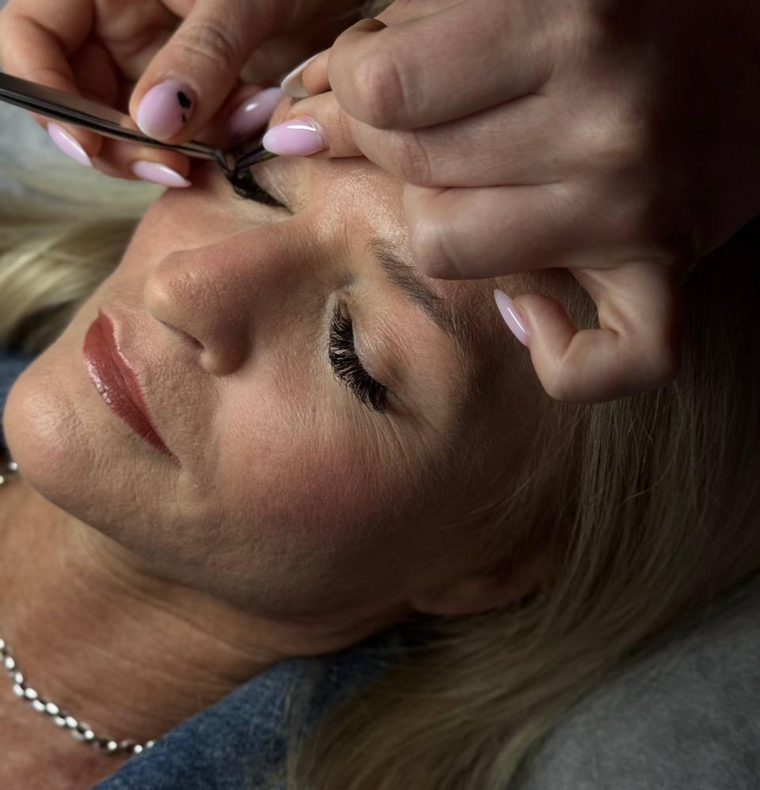 Close-up of an esthetician applying eyelash extensions to a woman's eye.