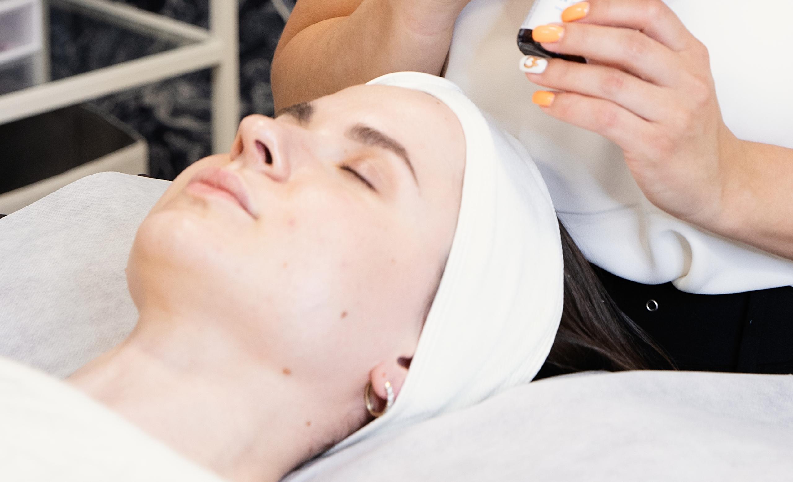 A skincare aesthetician looking down at a client lying on a spa bed.