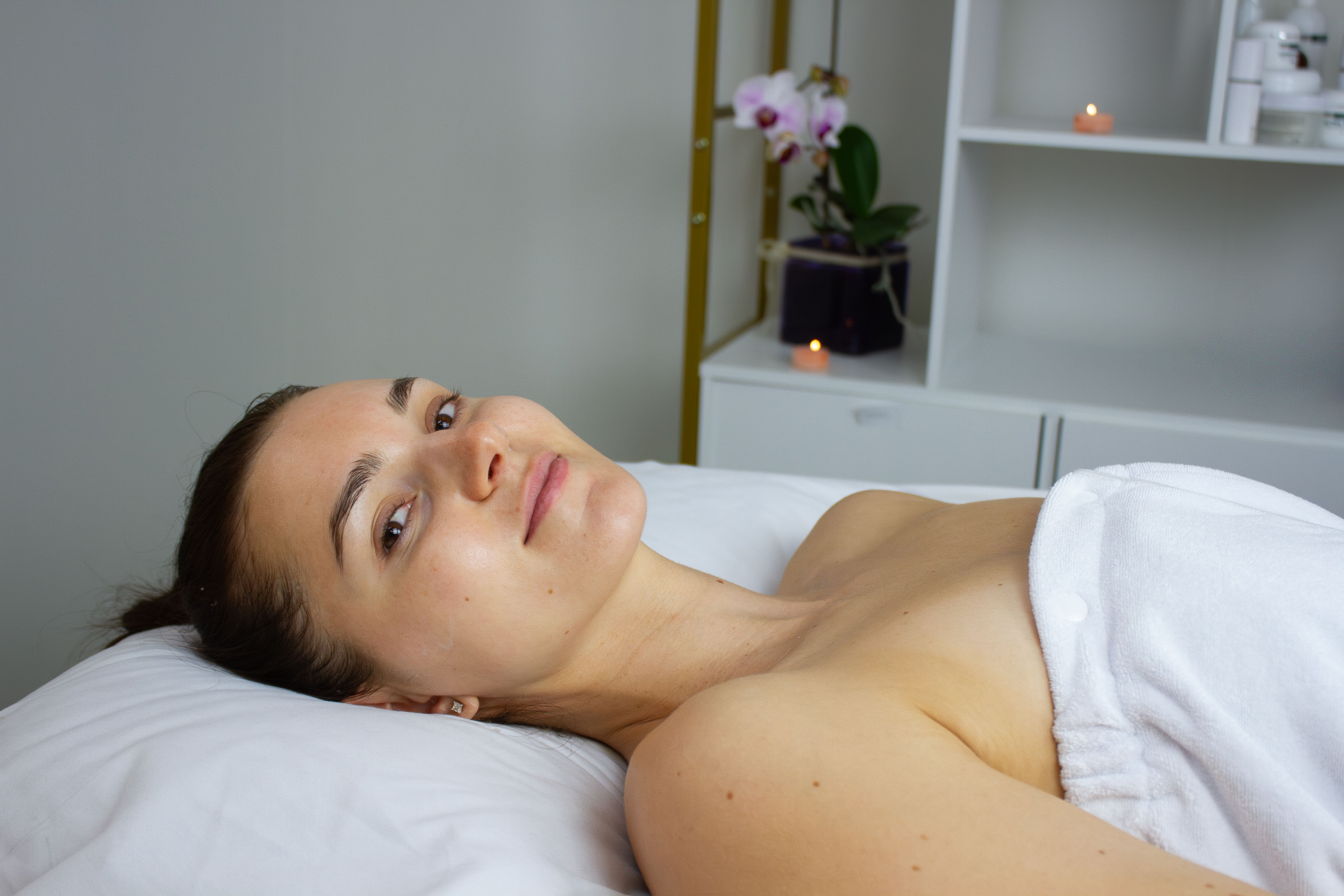 Woman with a gentle smile relaxing on a white spa table, covered in a towel.