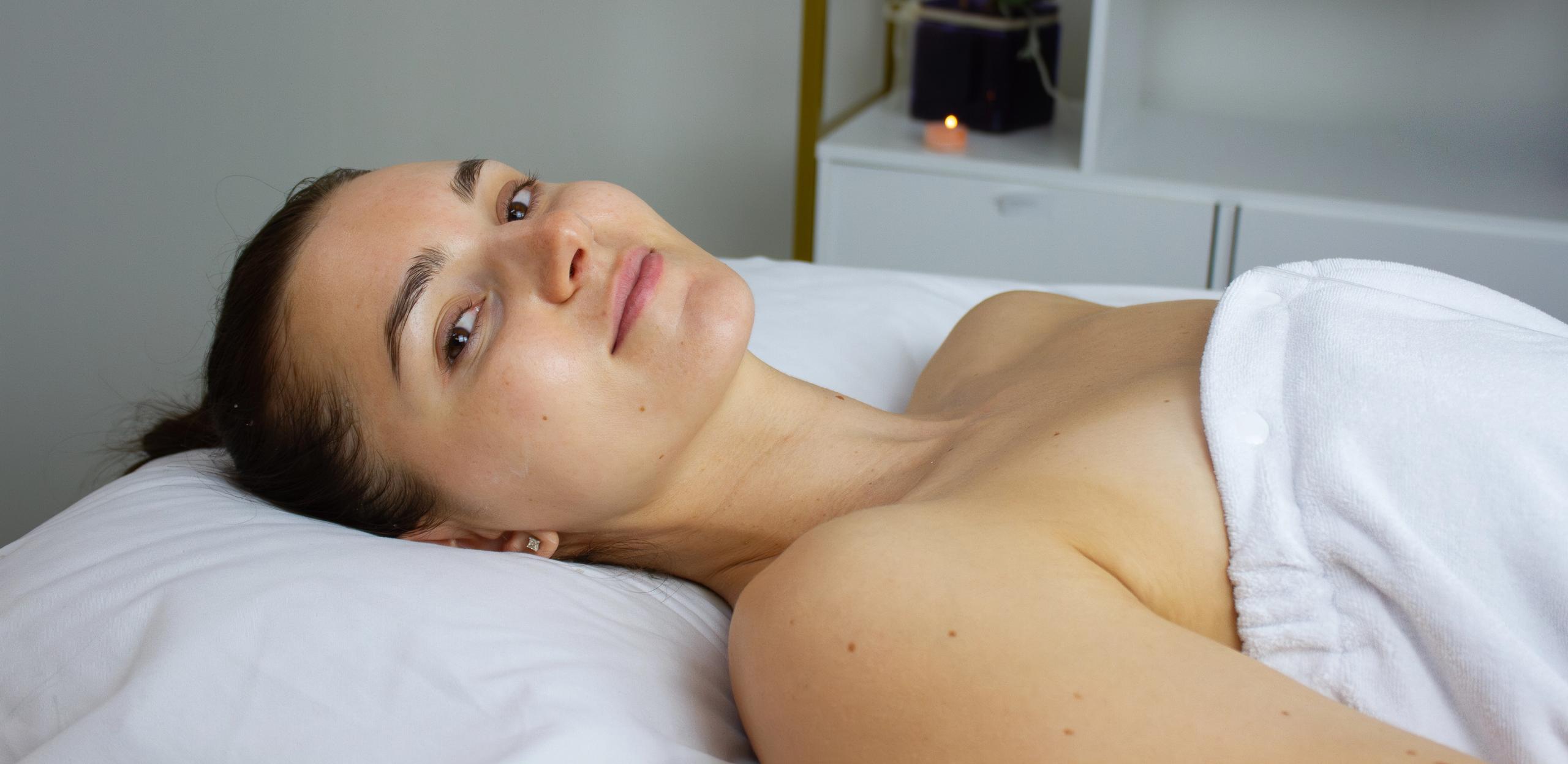 Woman with a gentle smile relaxing on a white spa table, covered in a towel.