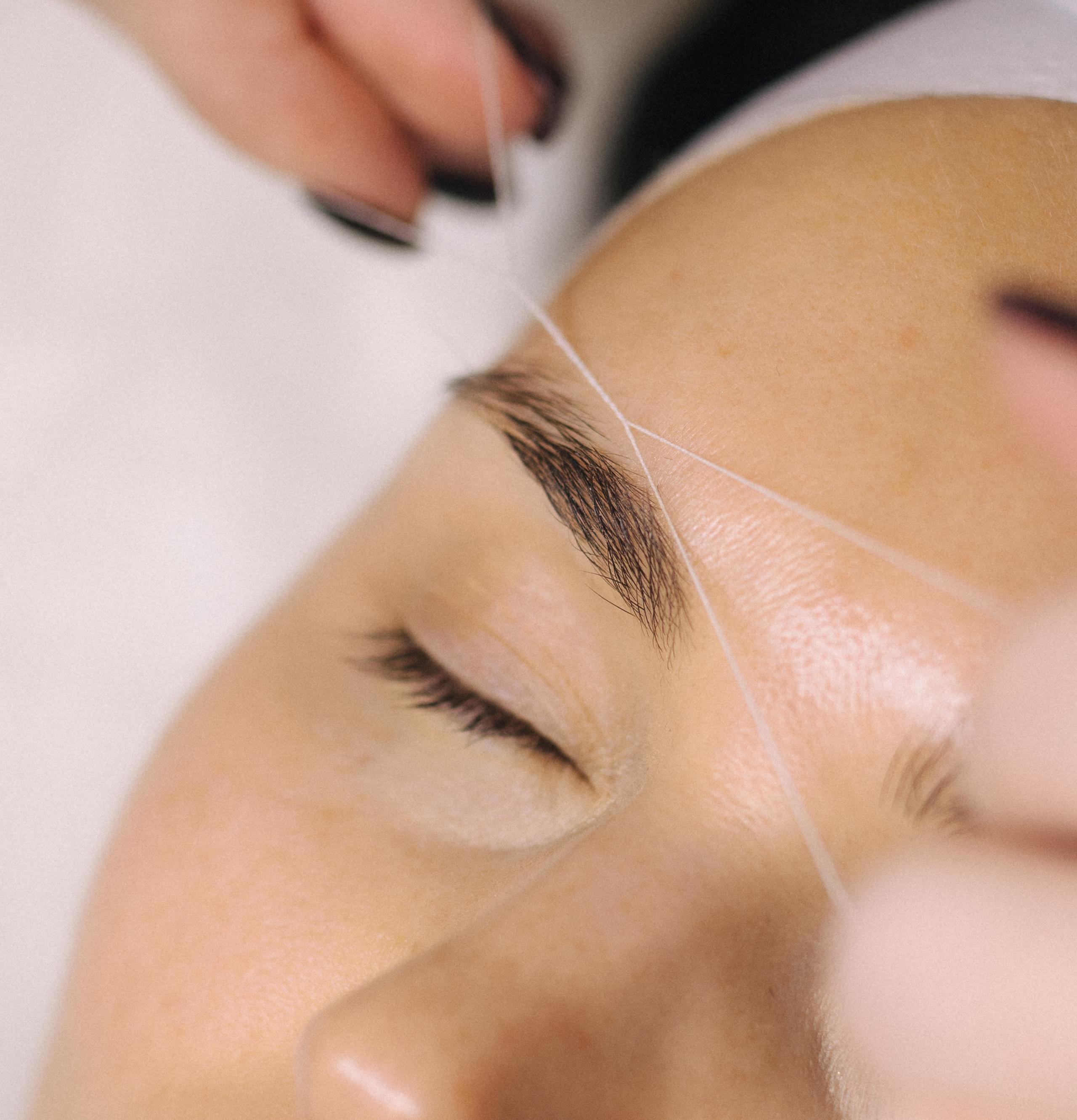Close-up of hands threading an eyebrow.