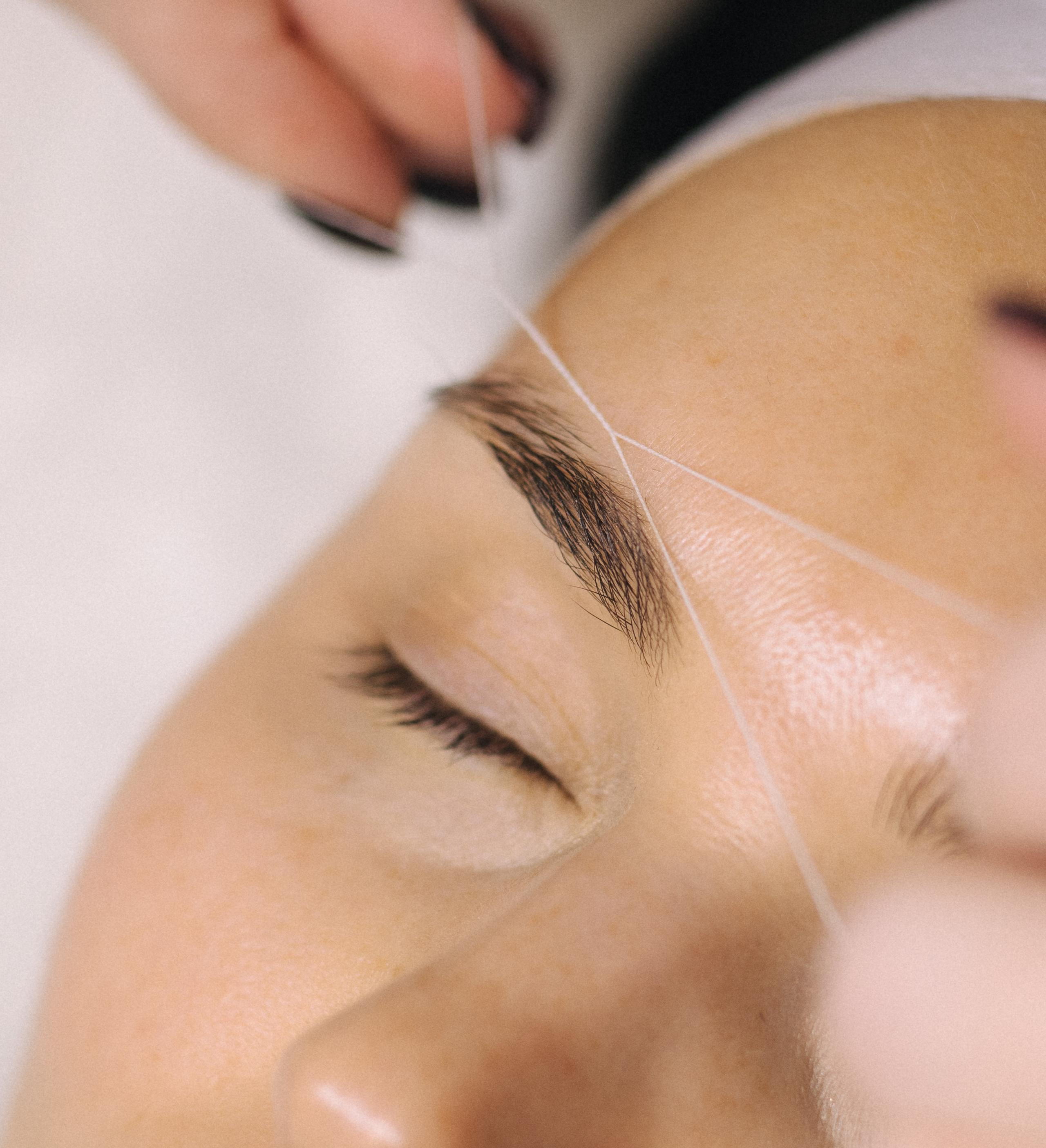 Close-up of hands threading an eyebrow.