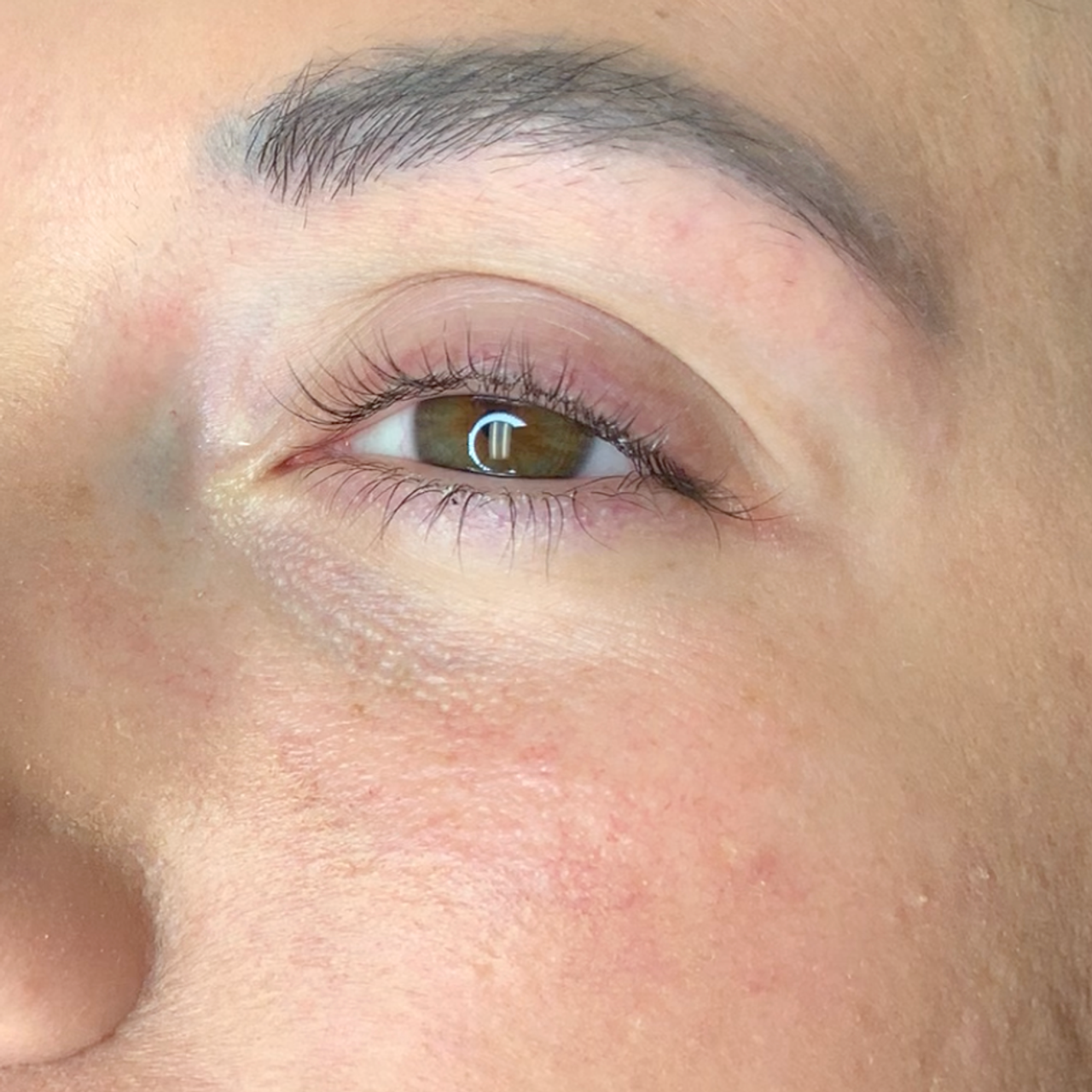 Close-up of a person's eye with a brown iris, curled eyelashes, and natural eyebrow.