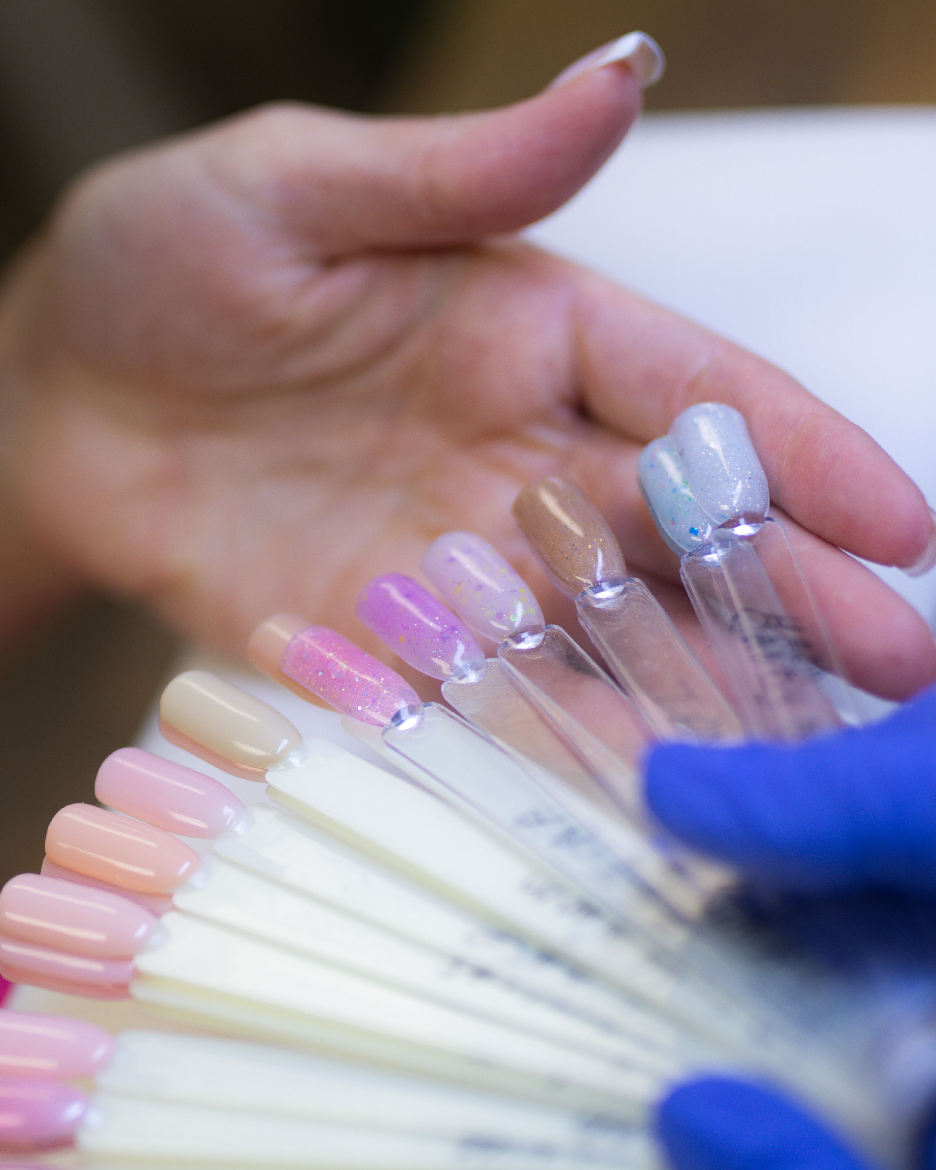 A client's hand selecting from a fan of diverse nail polish samples, presented by a gloved hand.