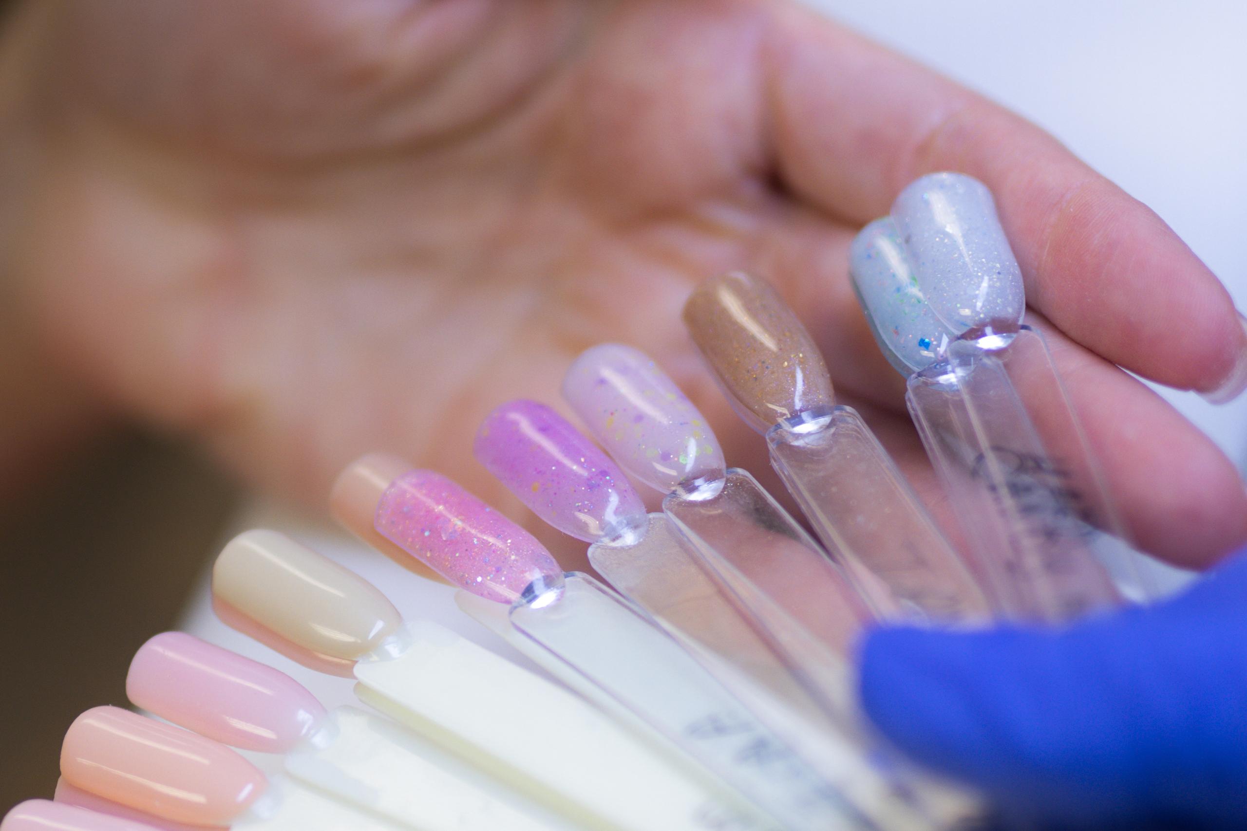 A client's hand selecting from a fan of diverse nail polish samples, presented by a gloved hand.