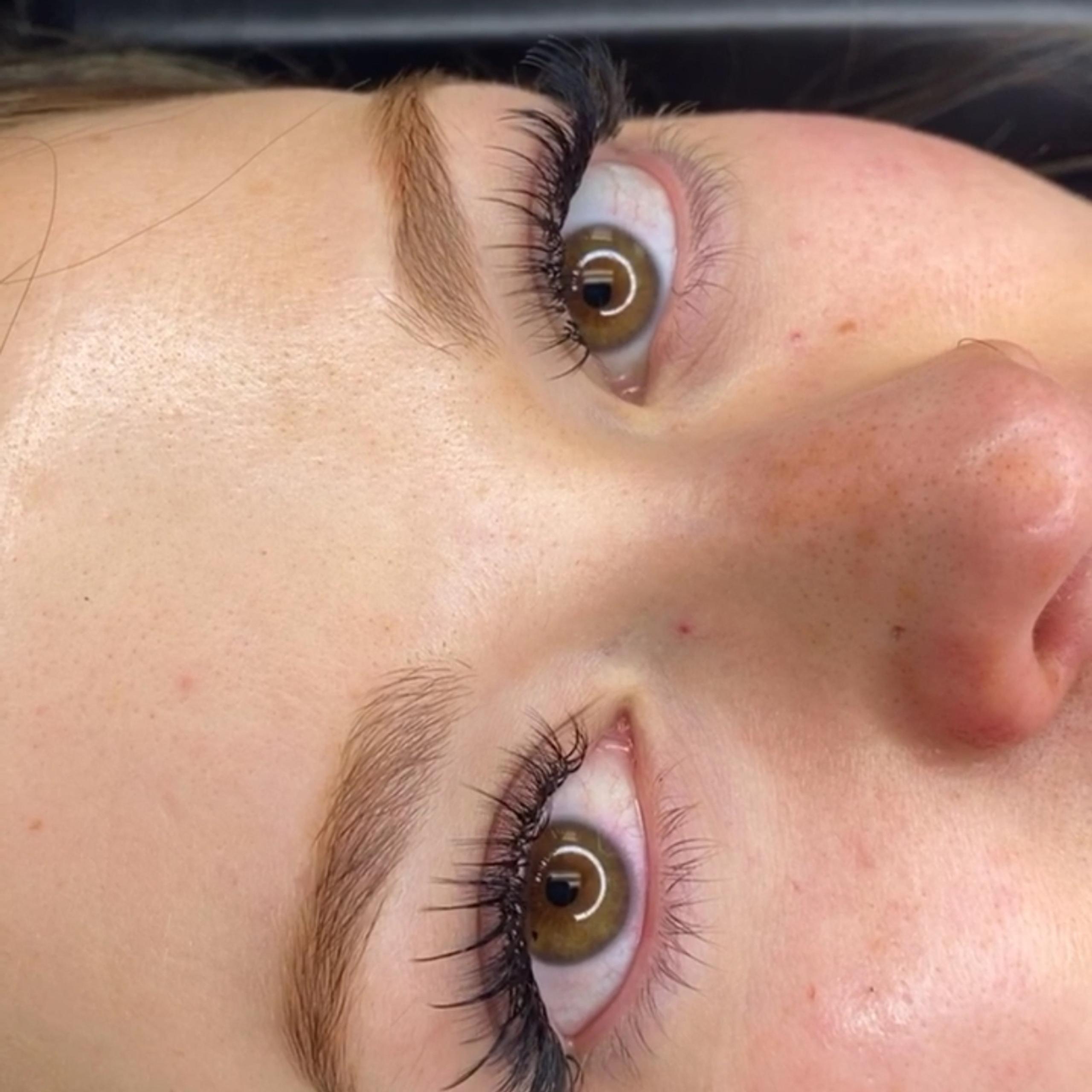 Close-up of a person's face with long, curled eyelashes with wispy spikes and open brown-green eyes
