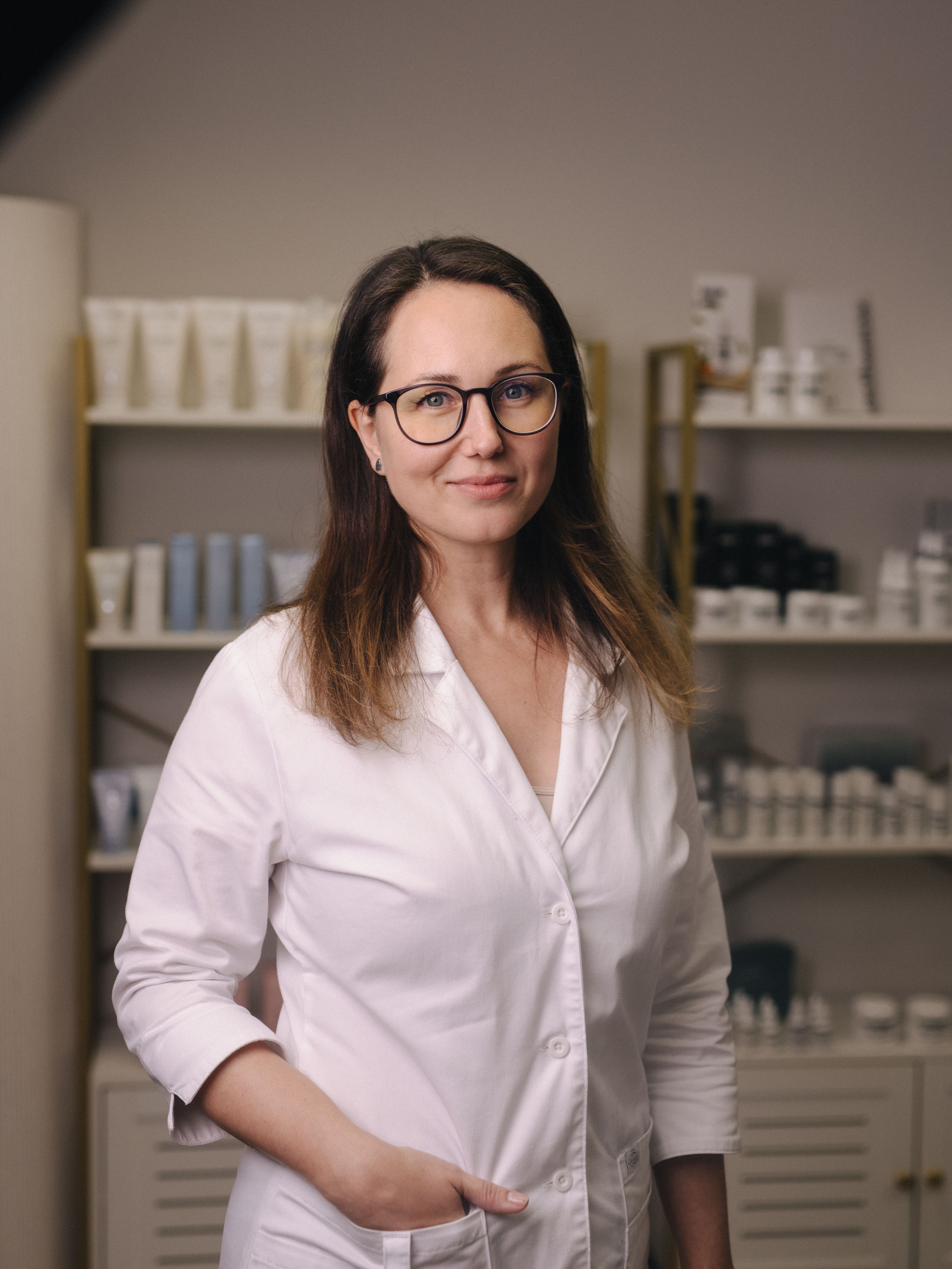A smiling woman in a white lab coat and glasses.