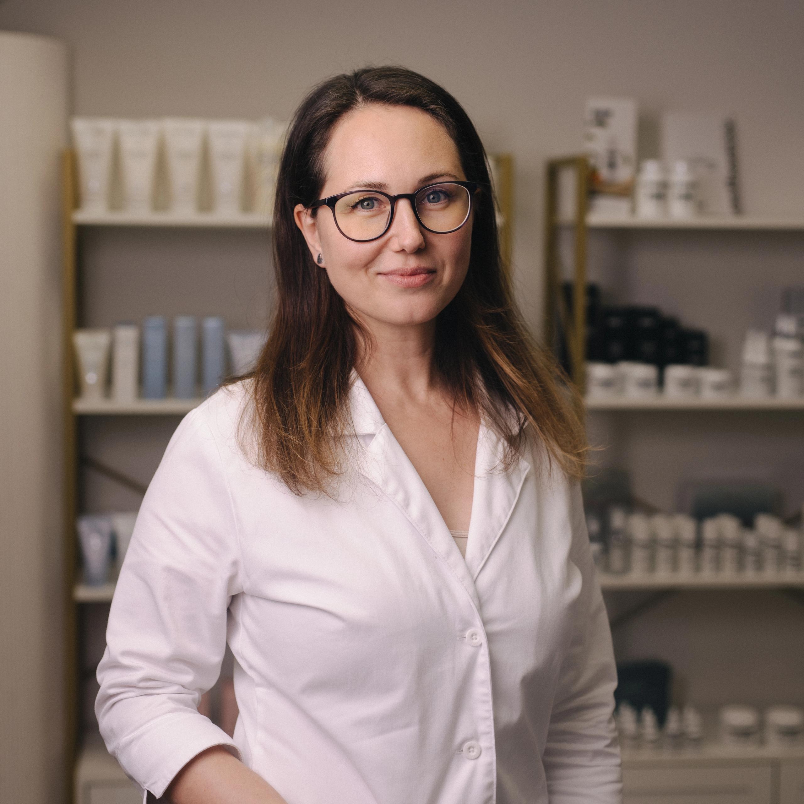A smiling woman in a white lab coat and glasses.