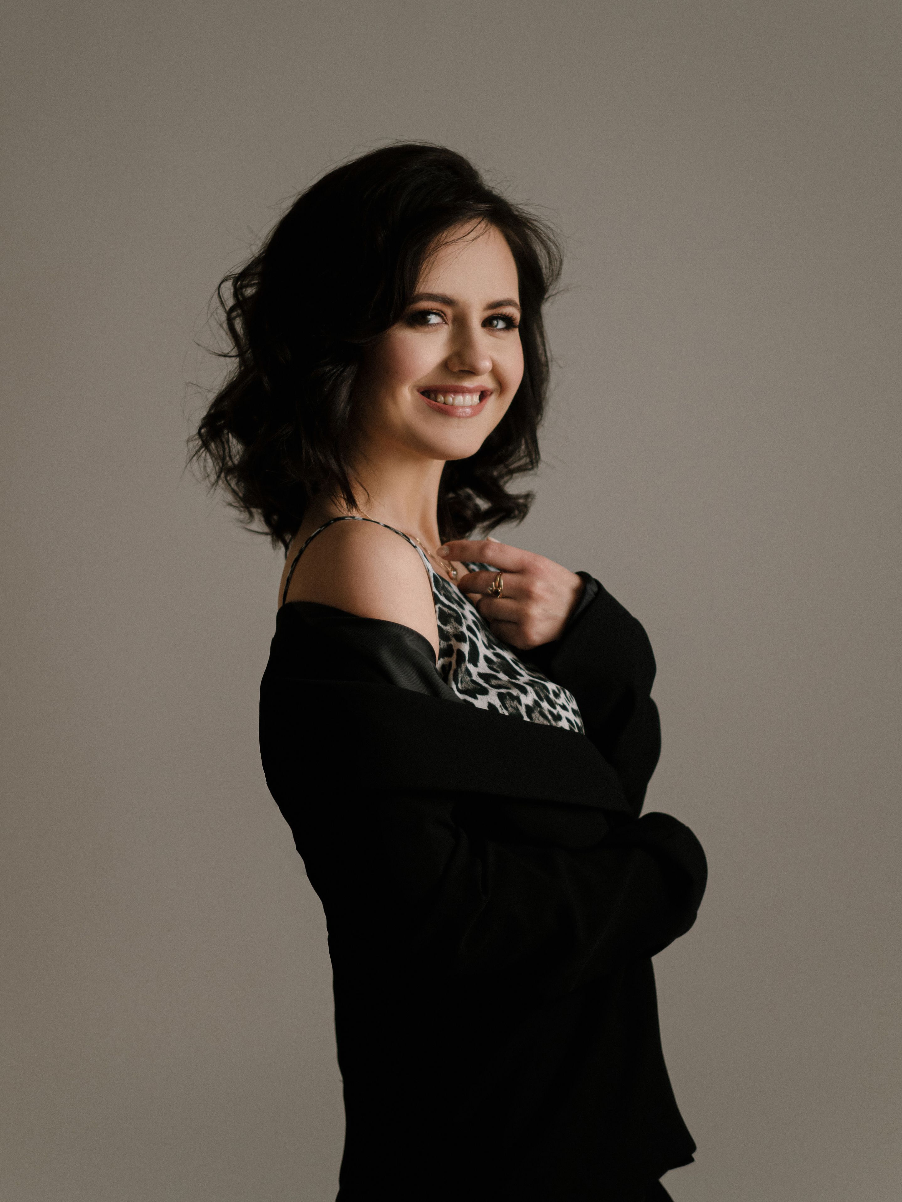 Smiling woman with dark wavy hair in a black blazer and leopard print top.