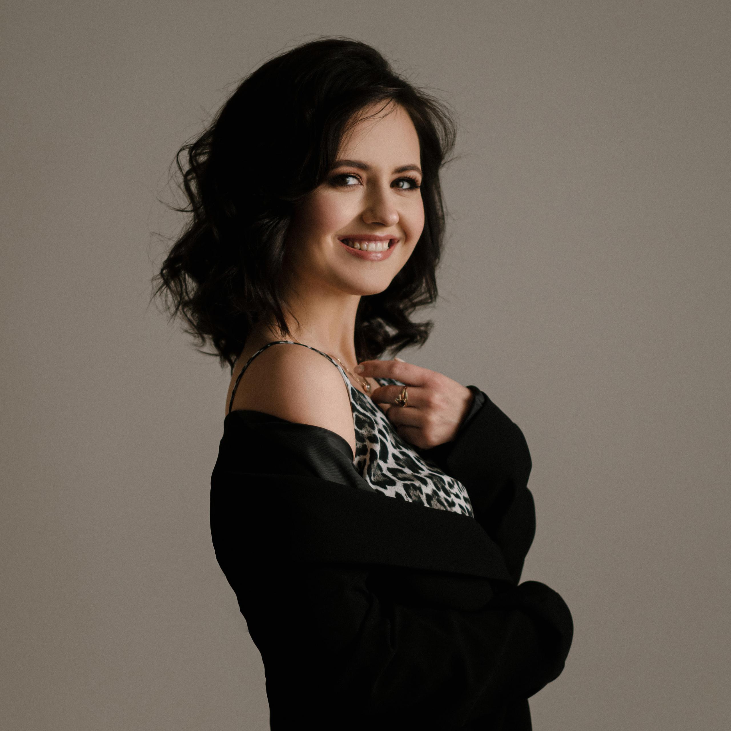Smiling woman with dark wavy hair in a black blazer and leopard print top.