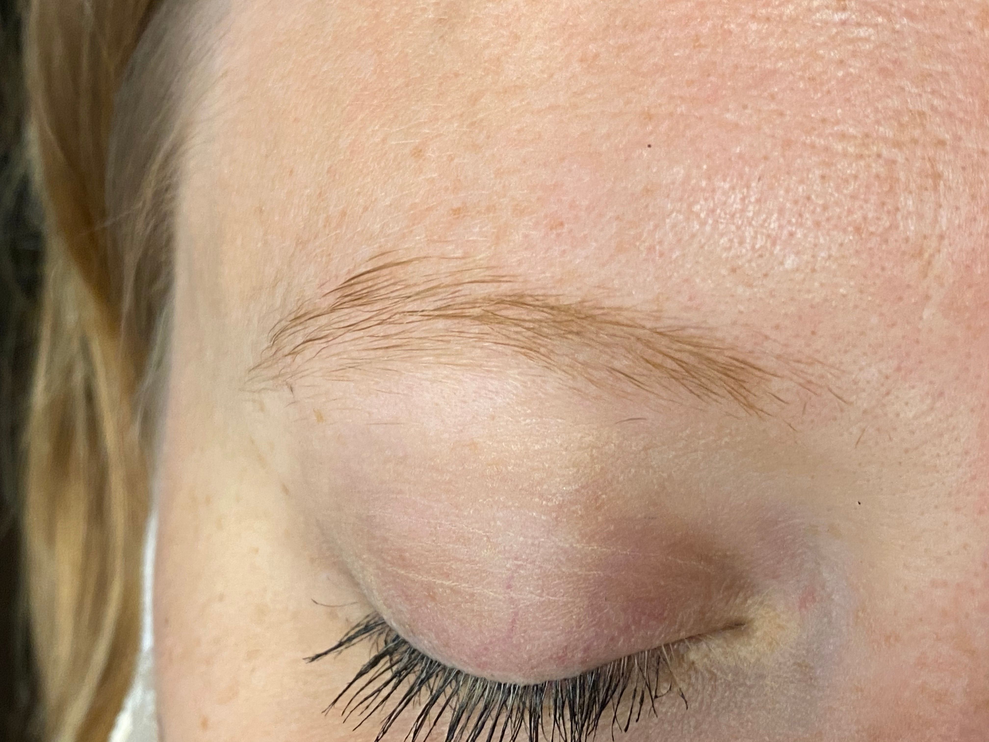 A close-up of a closed eye with a light brown eyebrow and dark eyelashes.